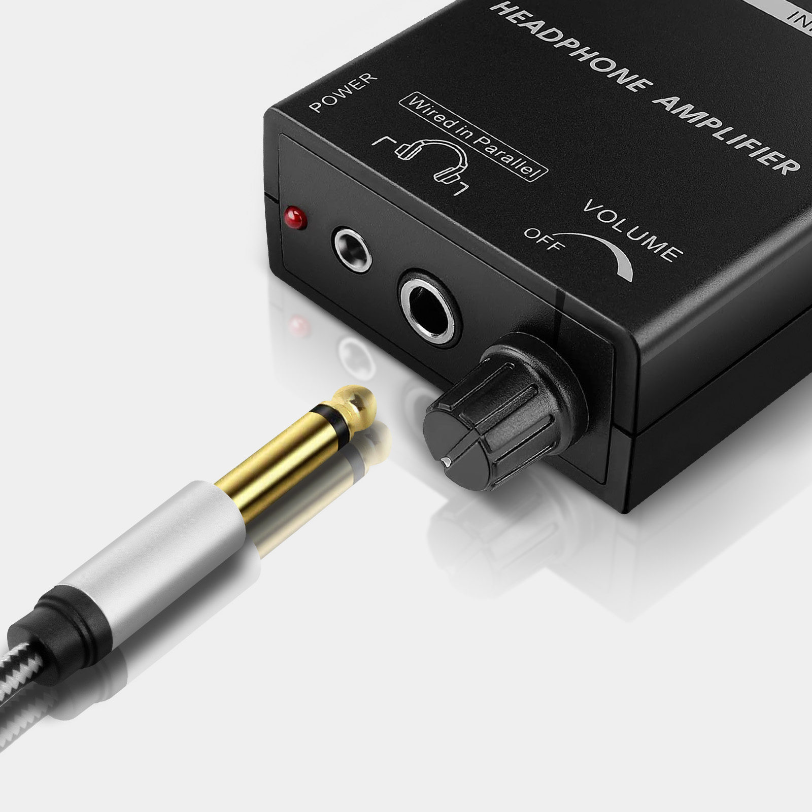 Amplificador de auriculares negro con mando de volumen y conector de audio, un cable de audio dorado y plateado está enchufado.