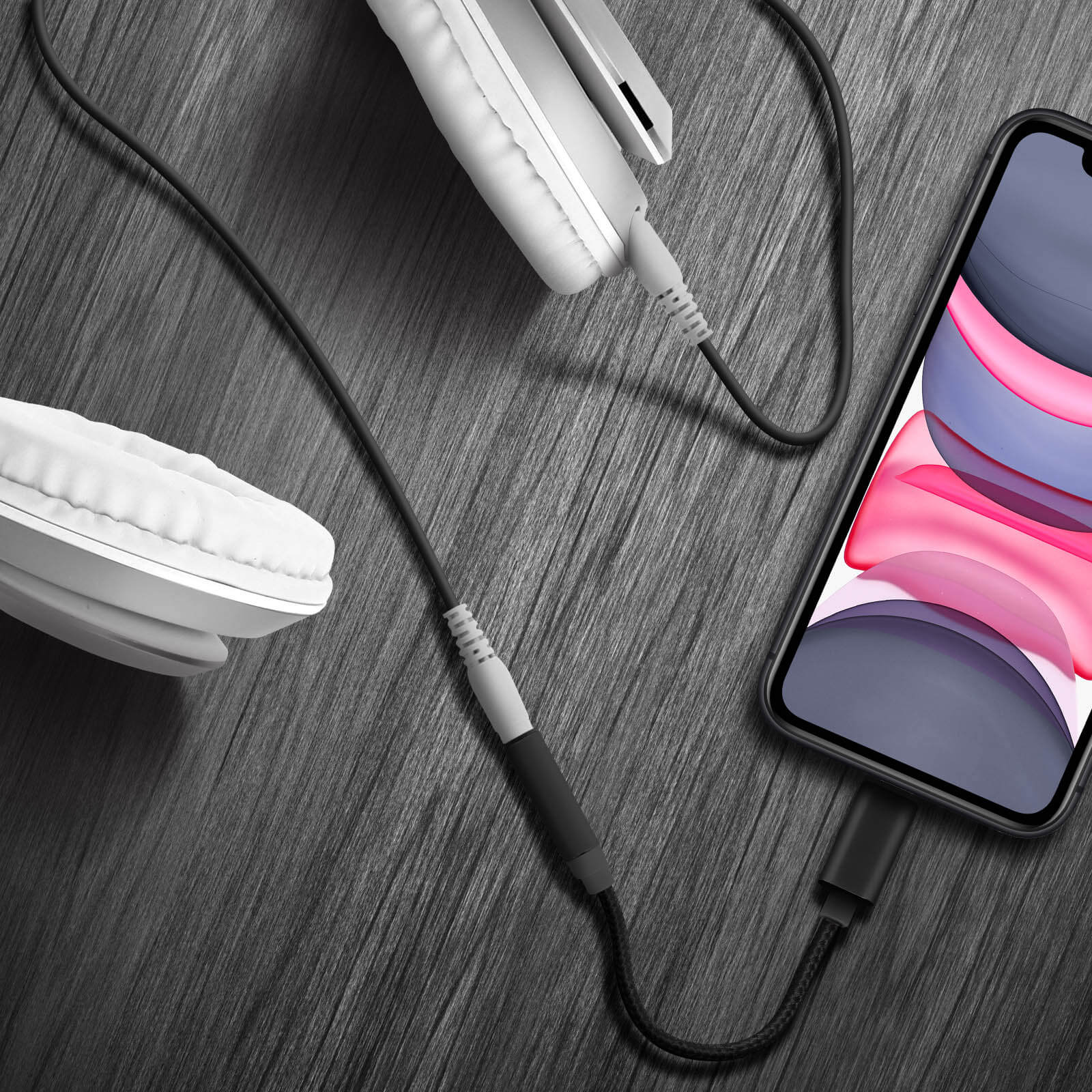 Cuffie, un telefono e un cavo su una superficie nera strutturata. Il cavo è collegato al telefono.