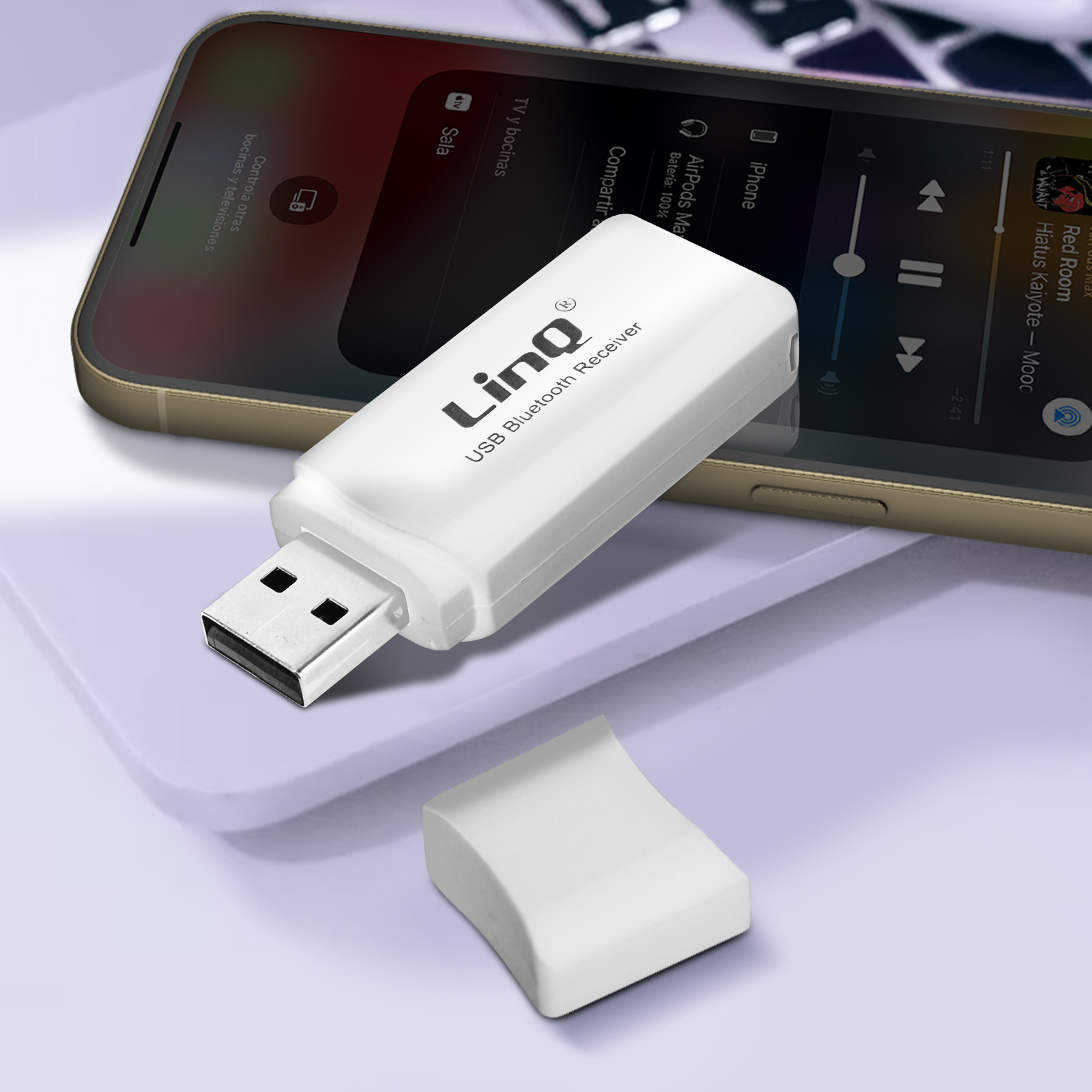 Un ricevitore Bluetooth USB bianco con una copertura accanto a un telefono. Il telefono è su un tavolo.