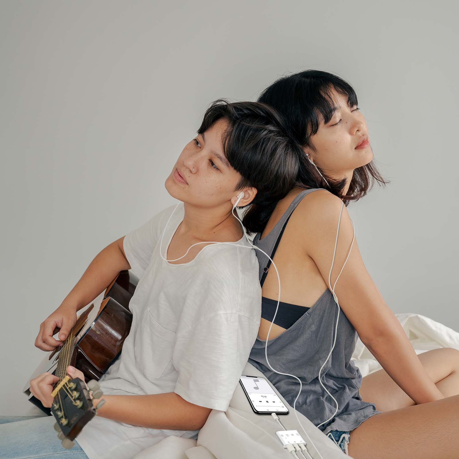 Due donne con cuffie, una suona la chitarra, un telefono con adattatore.