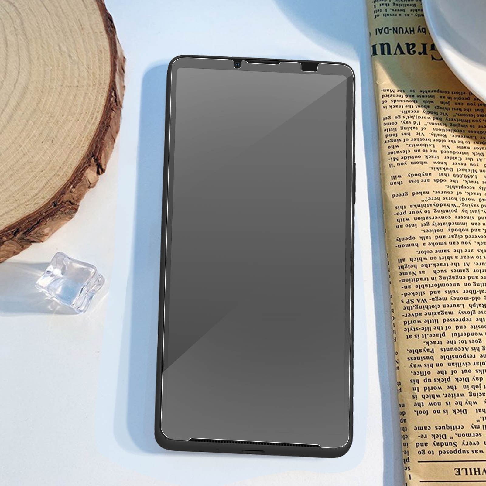 Telefoon met screenprotector aangebracht, op een wit oppervlak met een krantenachtergrond.