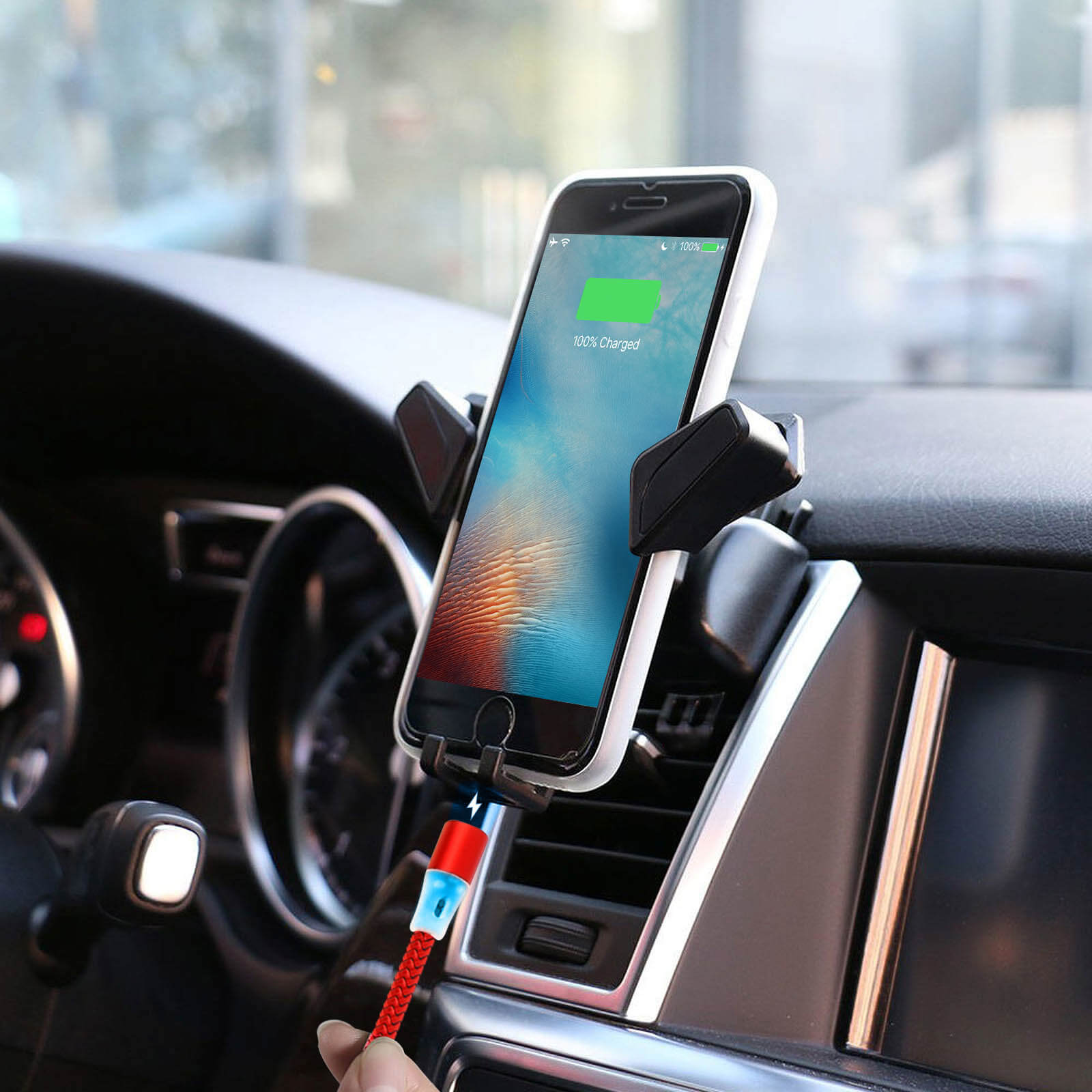Un telefono in carica in auto, collegato a un cavo rosso, con display carico al 100%.