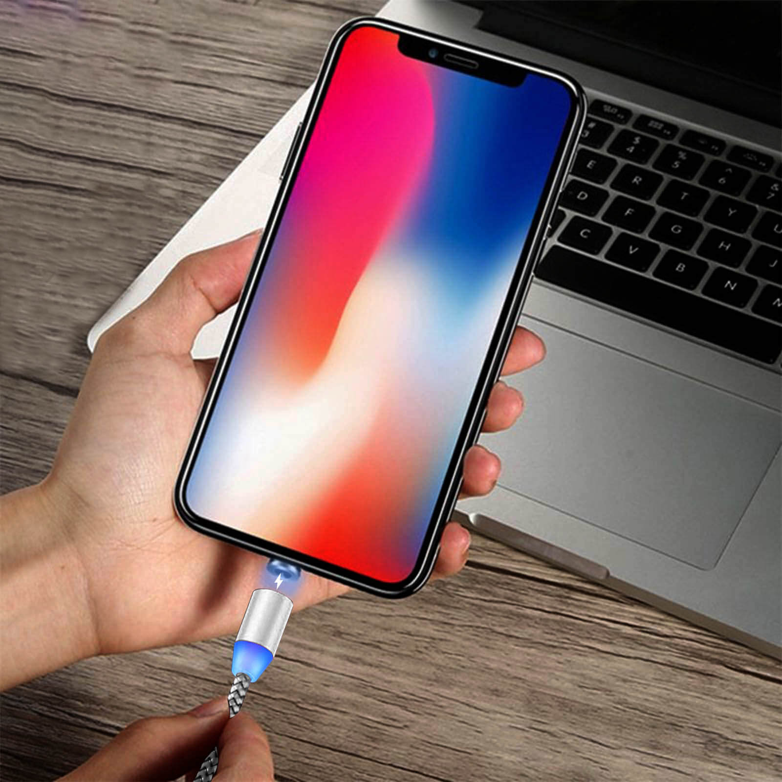 Une main tient un téléphone avec un écran coloré, connecté à un câble de chargement.