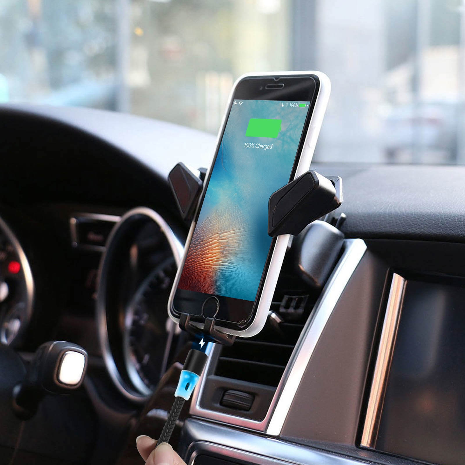 Un telefono in un supporto per auto, in carica con un cavo. Il telefono mostra 100% carica.