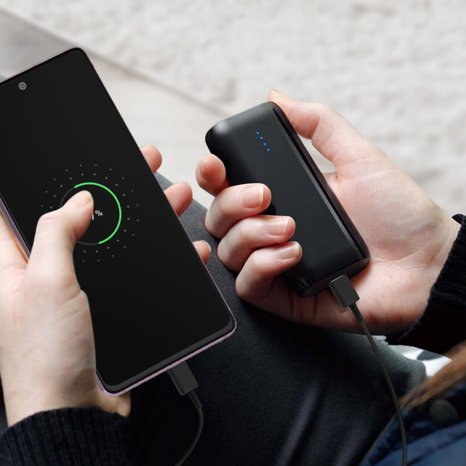 Un telefono in carica accanto a un power bank nero, tenuto in mano.