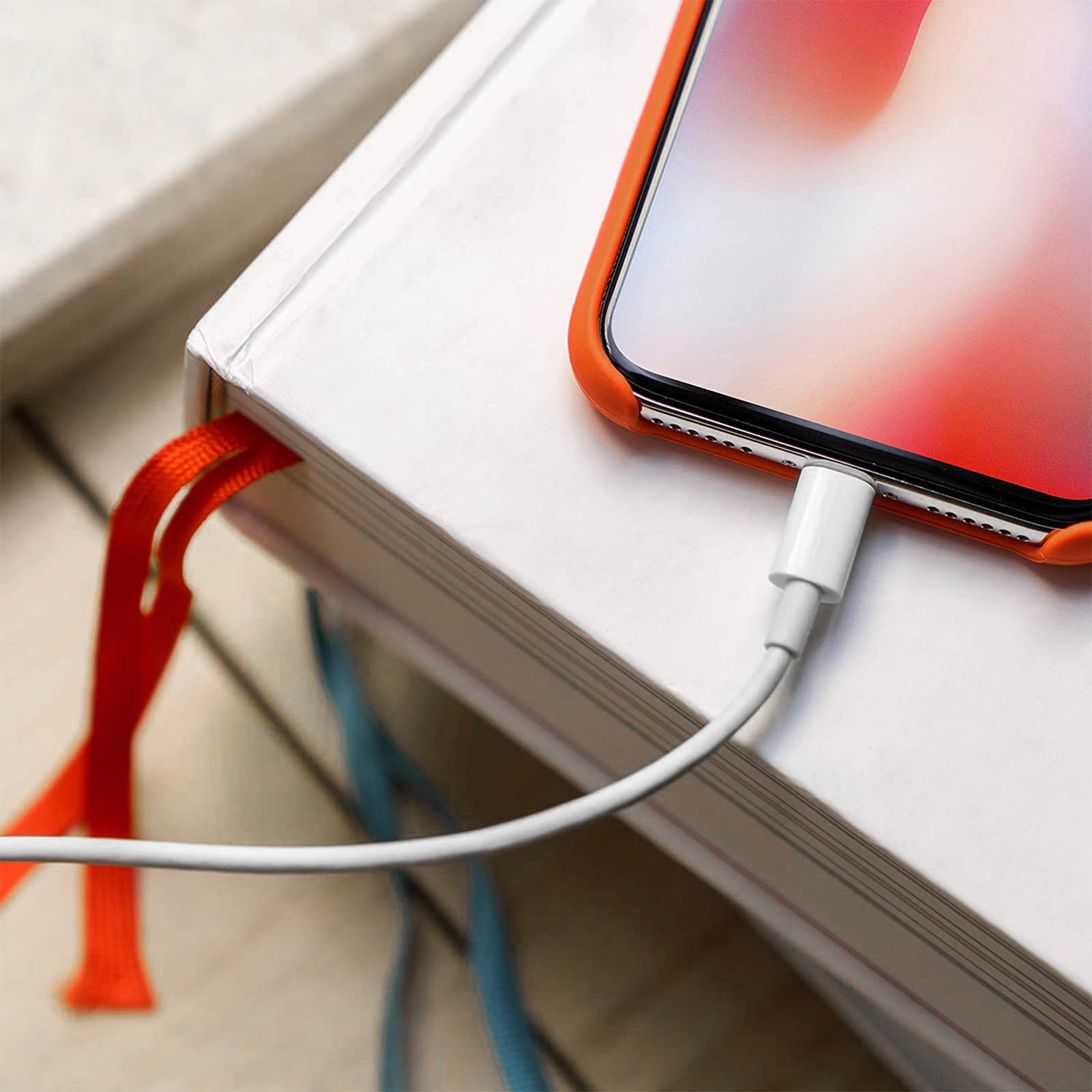 Un telefono in carica, collegato a un cavo bianco. Il telefono è su un libro bianco con un nastro arancione.