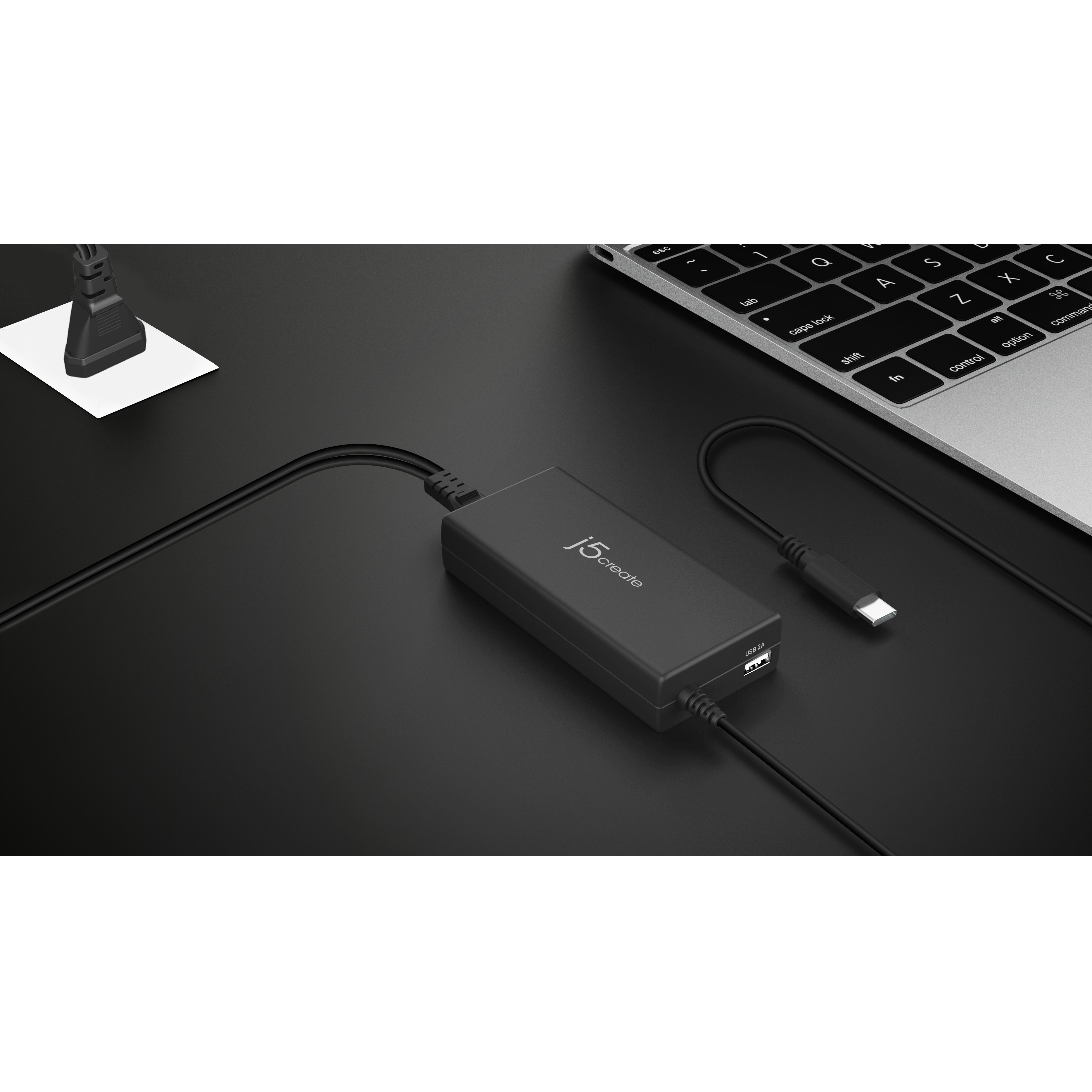 Adaptador j5create negro conectado a un portátil sobre una superficie negra. Puertos USB y USB-C visibles.