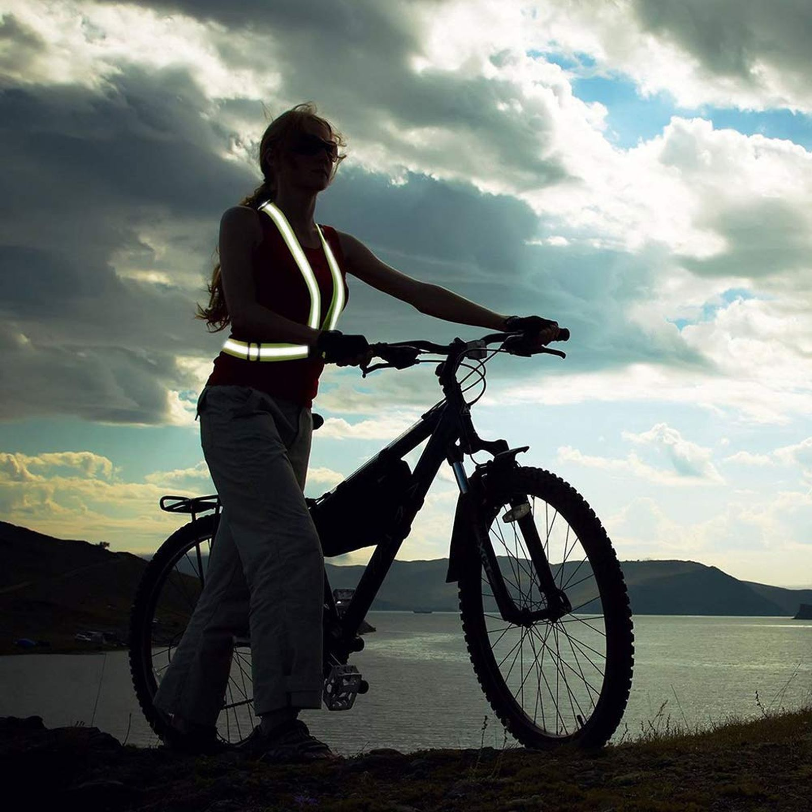 Eine Frau auf einem Fahrrad mit reflektierender Weste, in der Nähe von Wasser.
