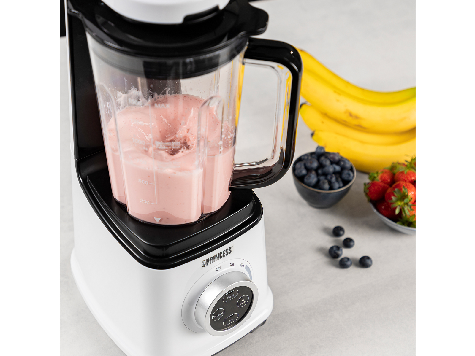 Un frullatore bianco e nero con un frullato rosa, circondato da frutta.