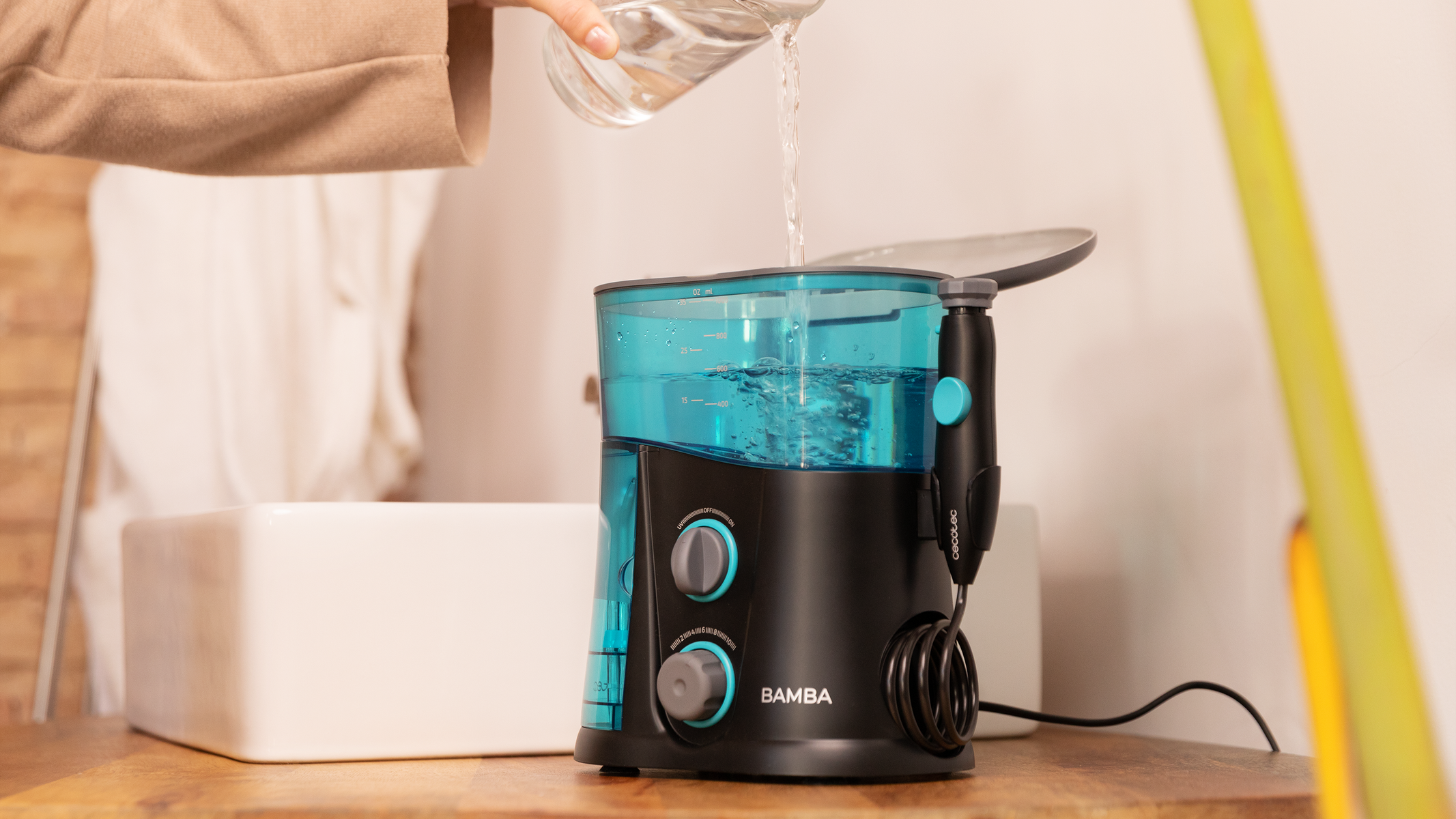 Een waterflosser die met water wordt gevuld, naast een wastafel in een badkamer.