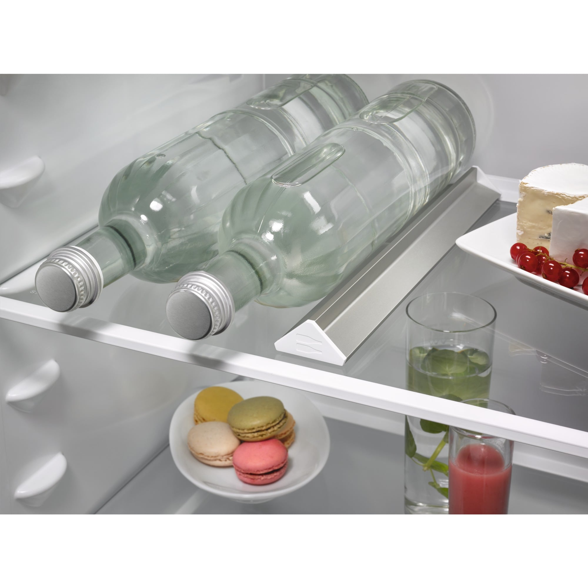 Koelkastplank met twee flessen water, een bord macarons en glazen.