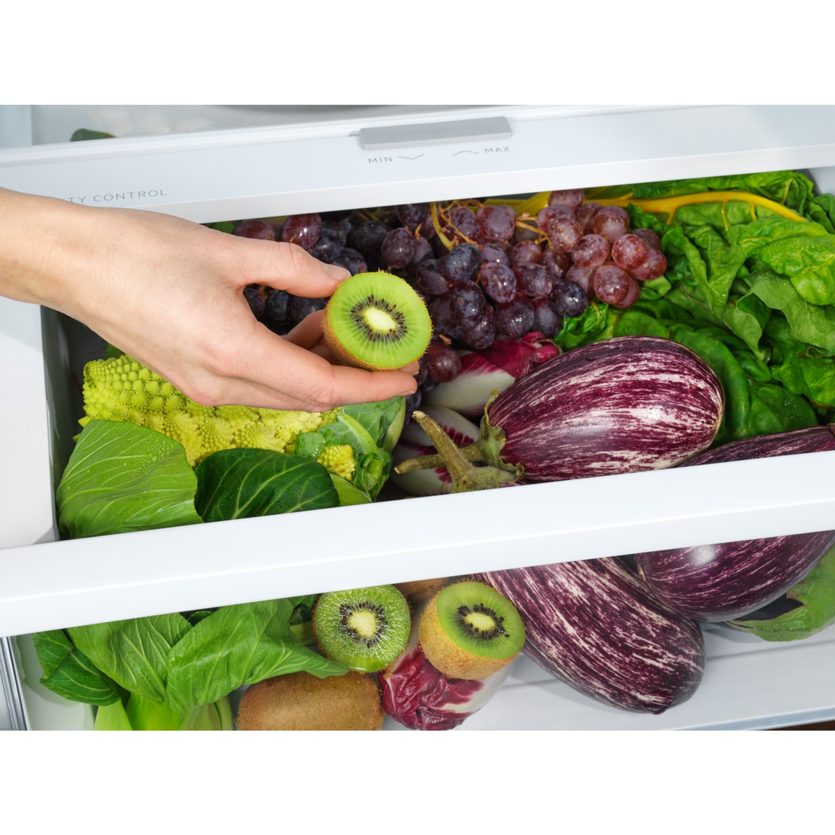 Hand die een in plakjes gesneden kiwi vasthoudt boven een koelkastplank vol producten.
