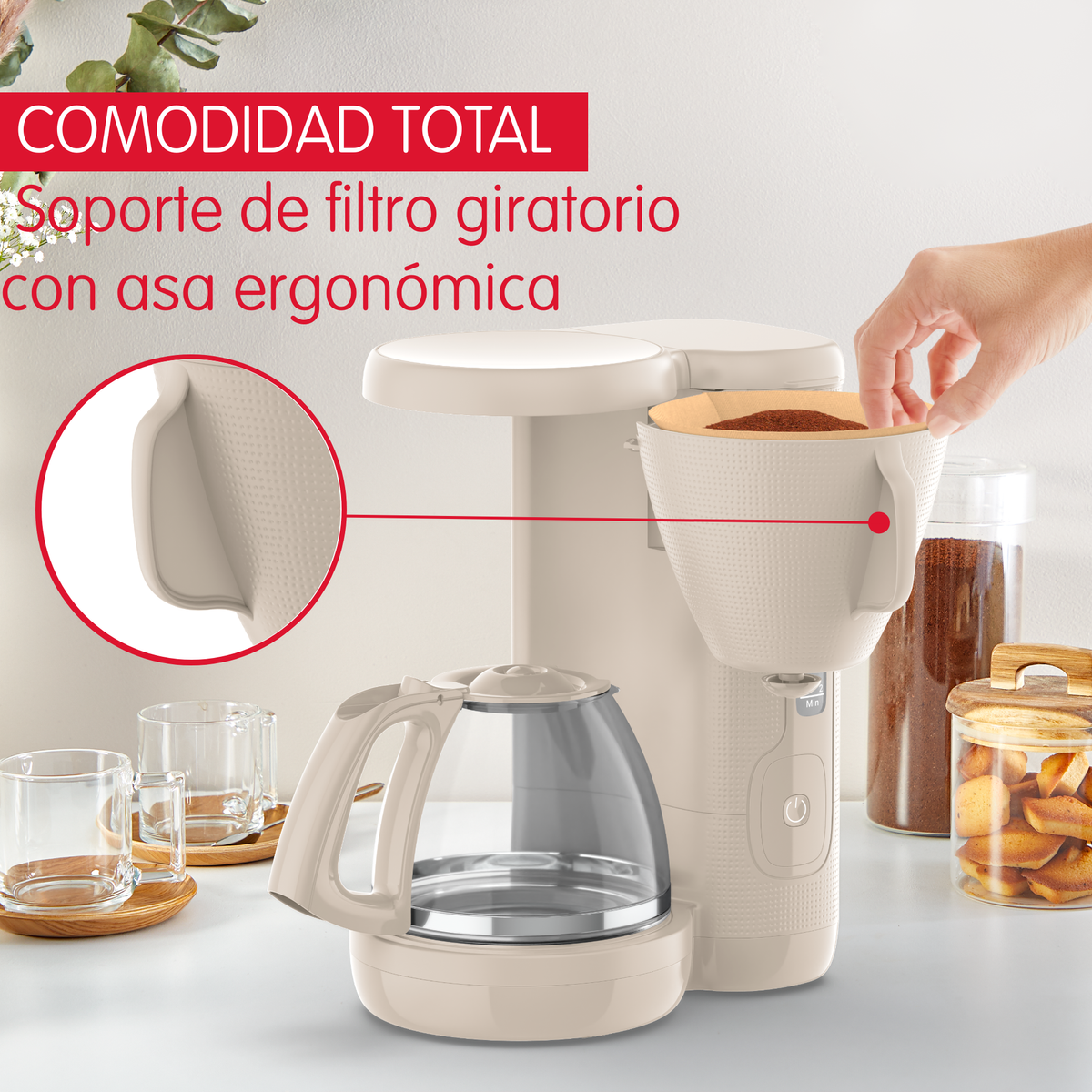 Macchina da caffè con caraffa in vetro. Una mano tiene un filtro. Altri oggetti sul bancone.