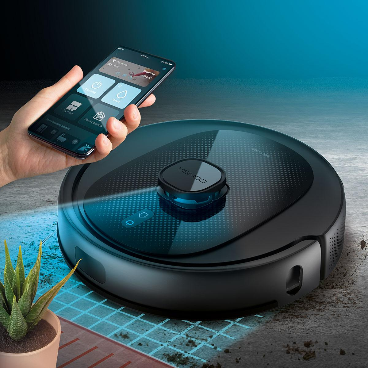 Un aspirateur robot avec un téléphone affichant son application, tenu par une main, sur une surface texturée.