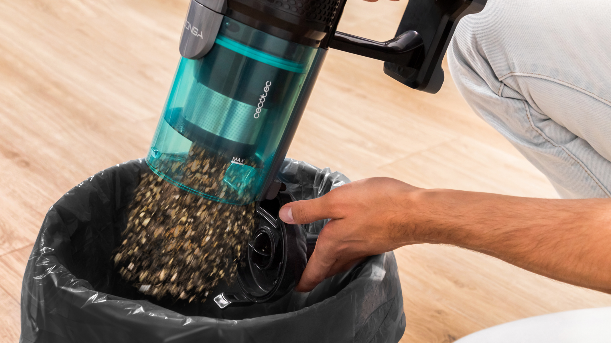 Osoba opróżniająca odkurzacz do worka na śmieci. Odkurzacz jest turkusowo-czarny.