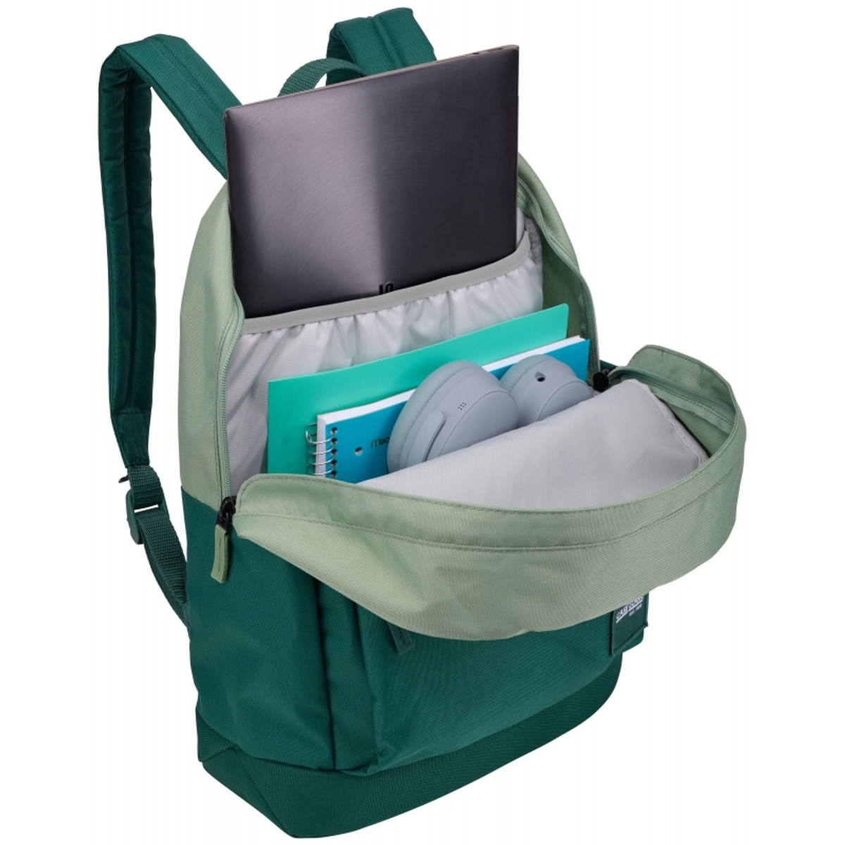 Grüner und dunkelgrüner Rucksack mit Inhalt: Laptop, Notizbücher, Kopfhörer und andere Gegenstände.