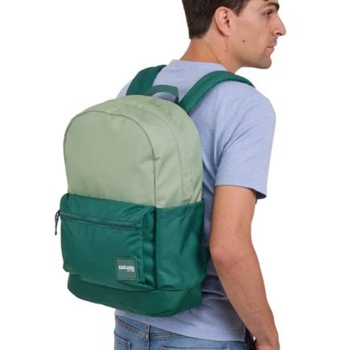 Mann mit grünem und hellgrünem Rucksack. Trägt blaues Hemd, Jeans. Weißer Hintergrund.