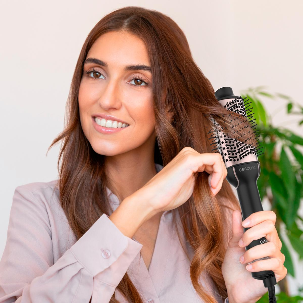 Donna che si acconcia i capelli con una spazzola nera e rosa. Sorridente, sfondo chiaro.