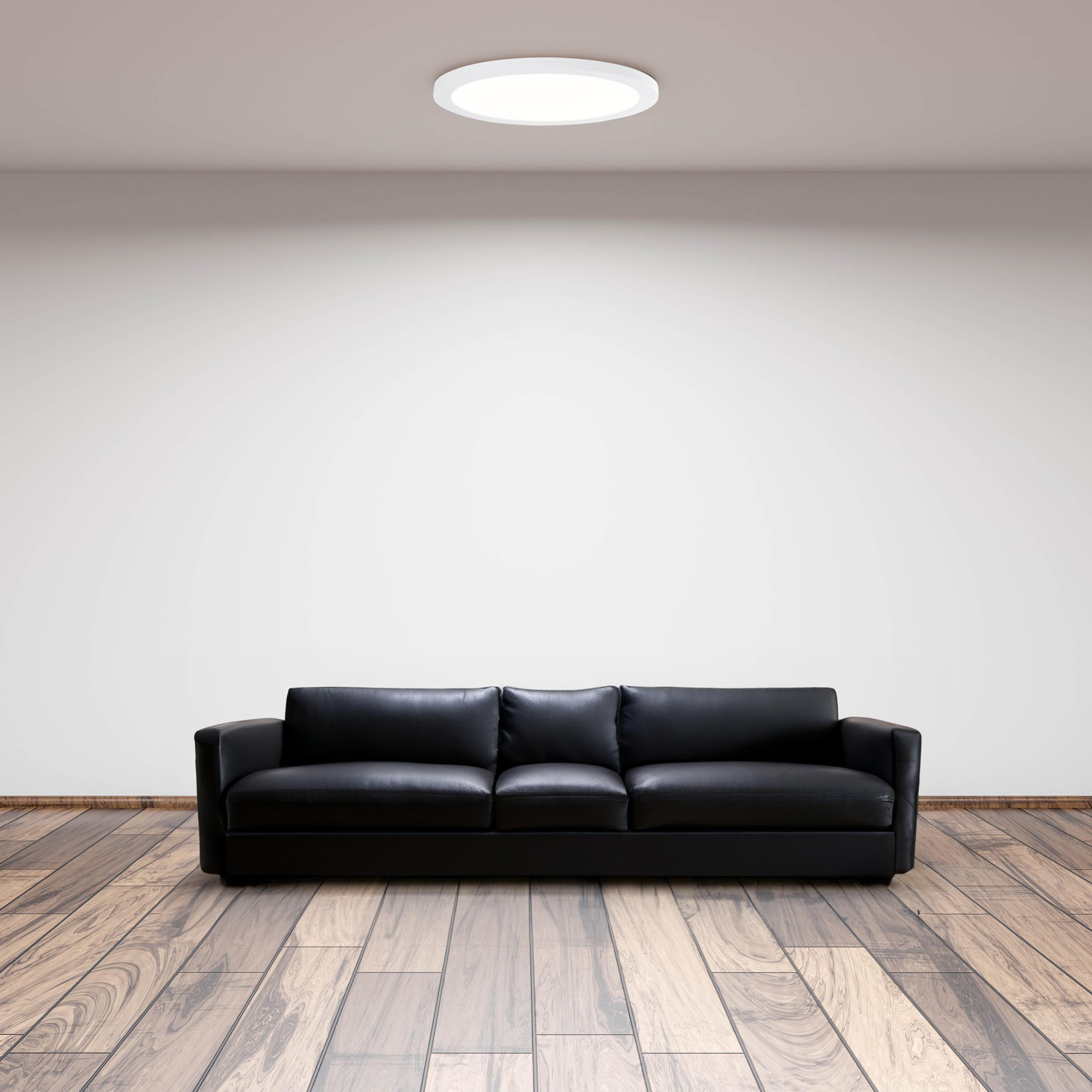 Ein schwarzes Sofa vor einer weißen Wand, mit Holzboden und Deckenleuchte.