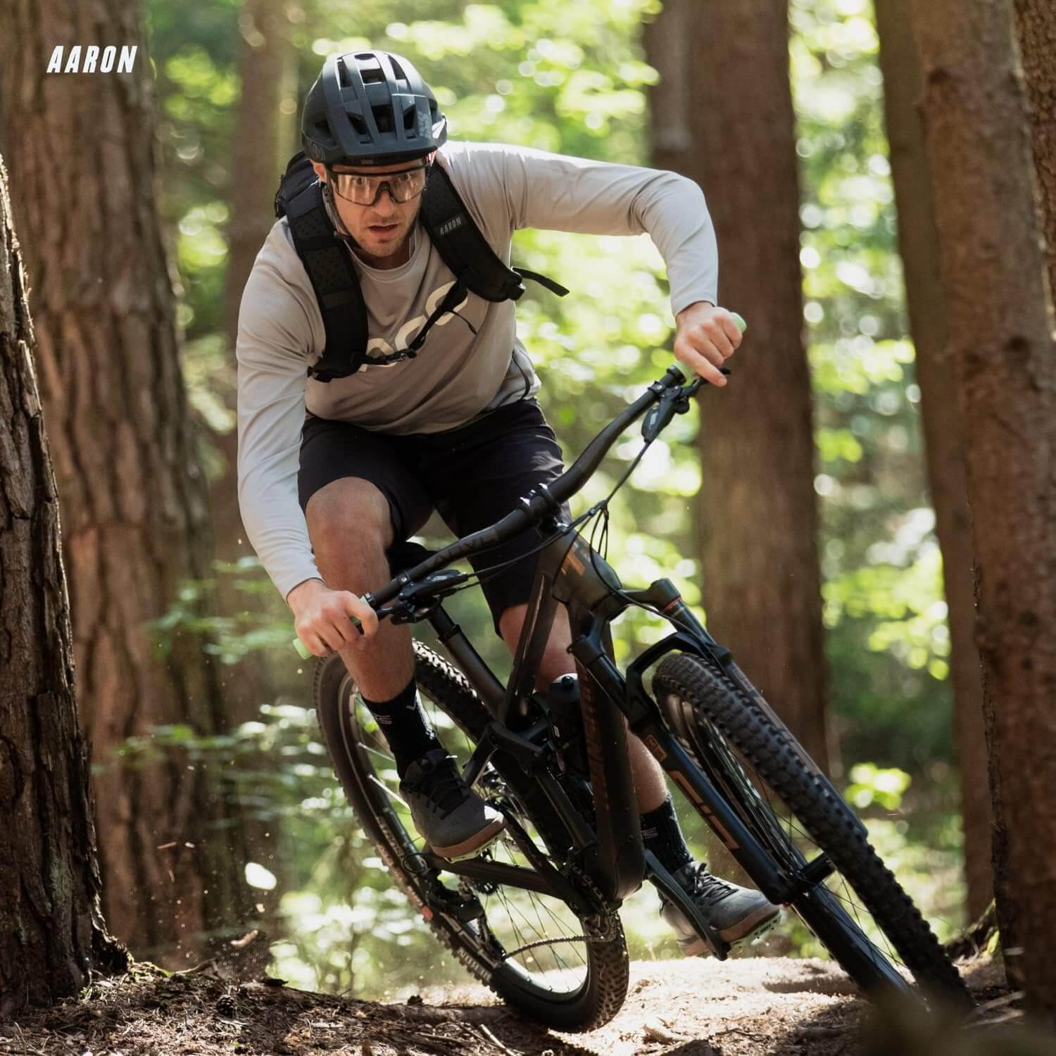 Mountainbiker fährt durch einen Wald, trägt Helm und Brille. Bäume im Hintergrund.