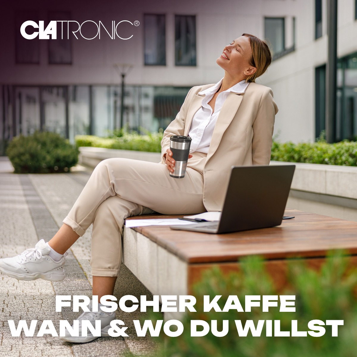 Kobieta w beżowym garniturze siedzi na ławce, trzymając filiżankę kawy i laptopa. Tłem jest budynek.