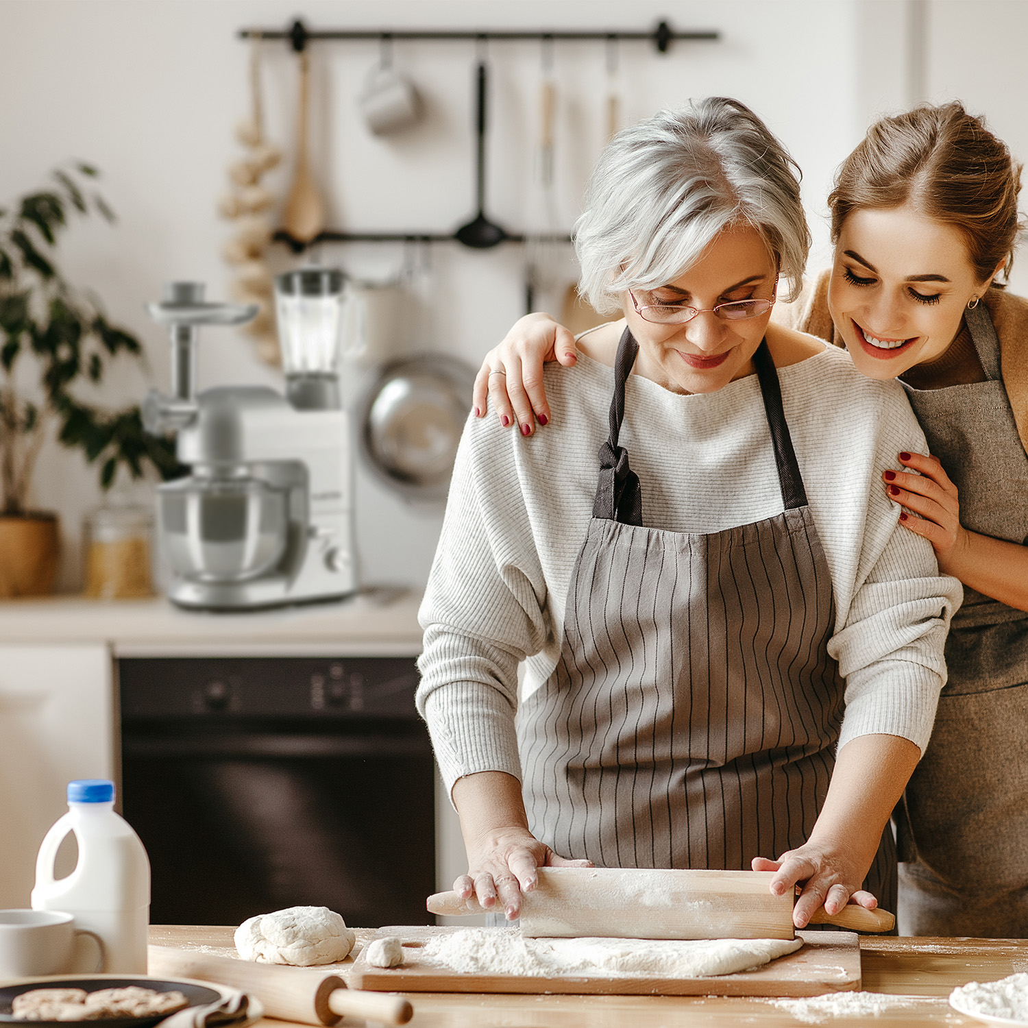Donna e donna anziana che cucinano insieme, con un robot da cucina sullo sfondo.