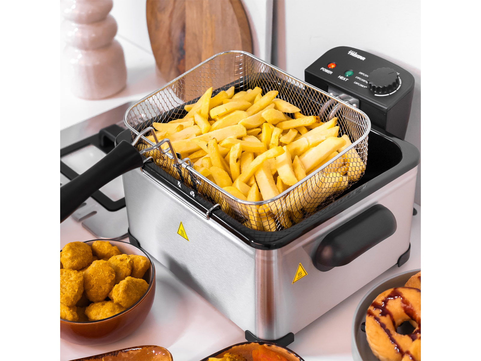 Una freidora de acero inoxidable con papas fritas dentro y otros alimentos en la encimera.