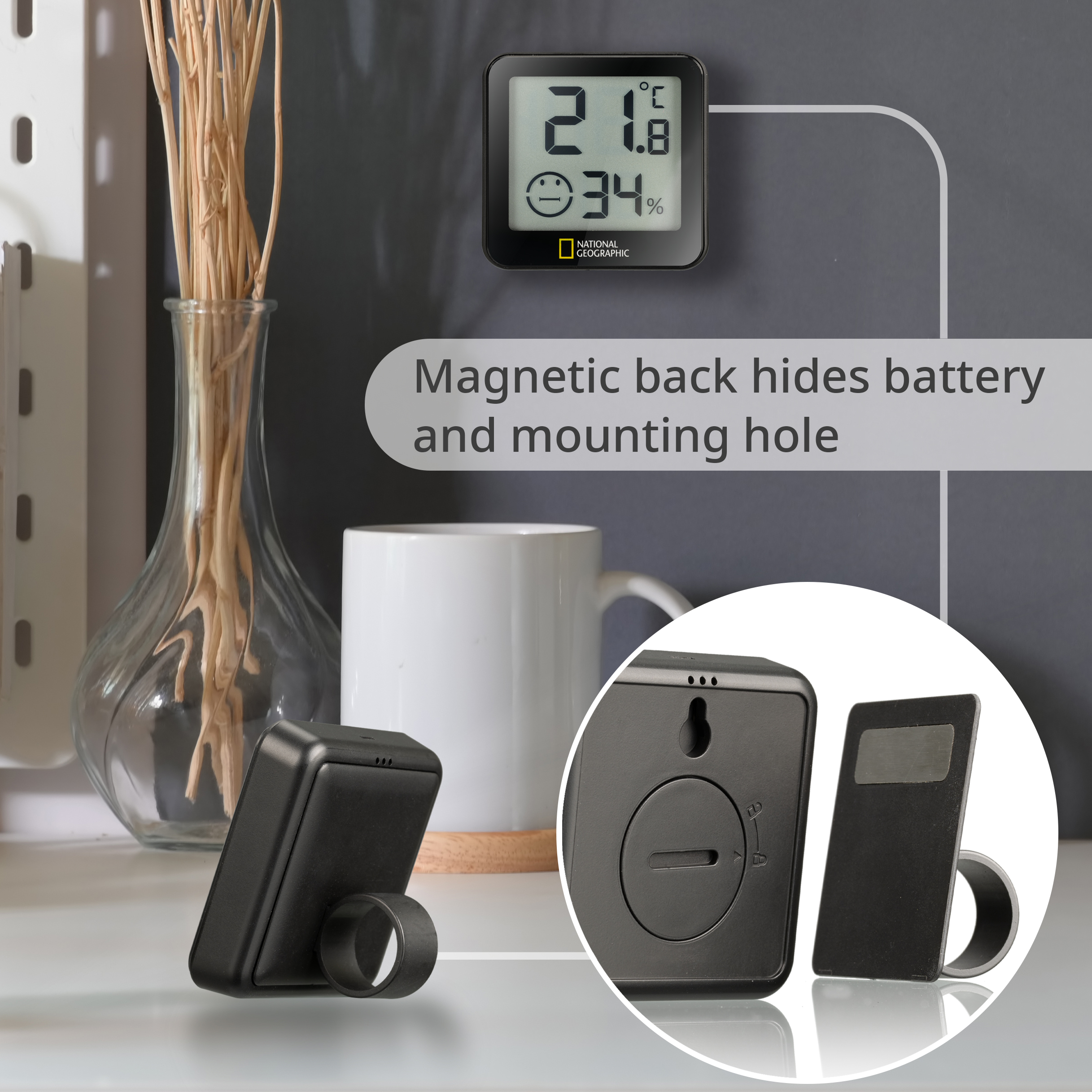 Ein schwarzes digitales Thermometer zeigt Temperatur und Luftfeuchtigkeit an. Tasse und Vase daneben.
