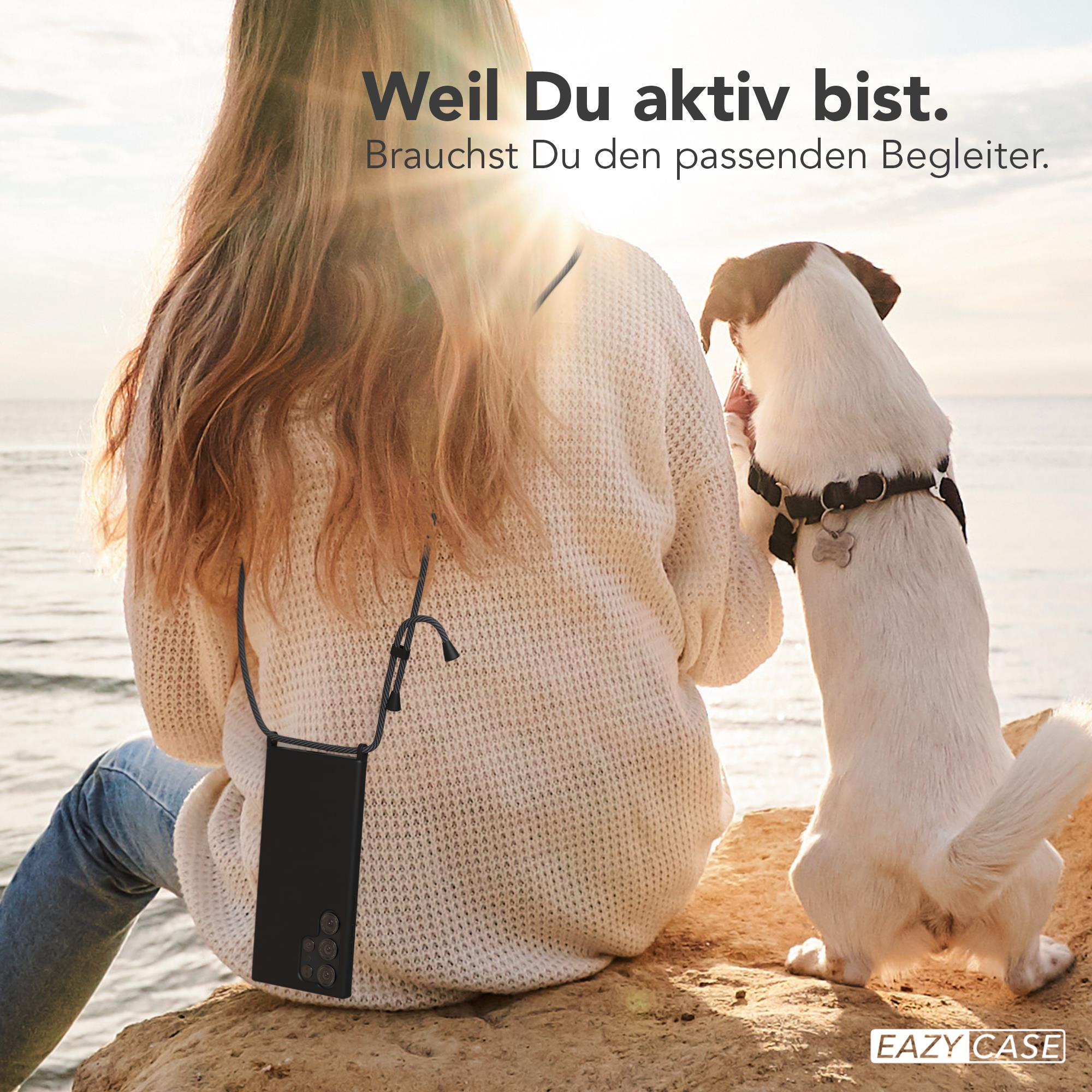 Frau und Hund am Strand, mit schwarzer Handyhülle um den Hals.