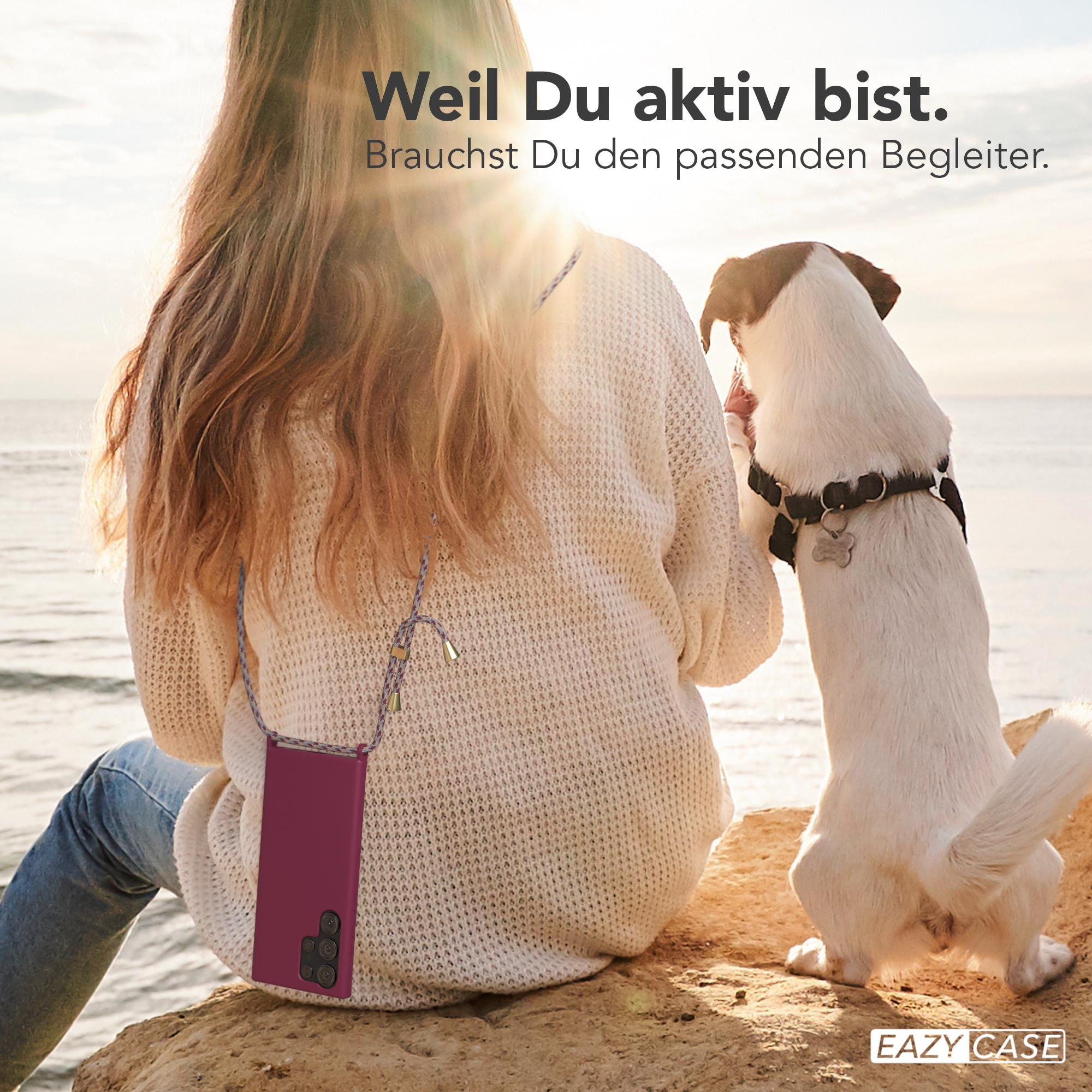 Frau mit Handyhülle und Hund am Strand. Die Hülle ist lila, der Hund weiß und schwarz.