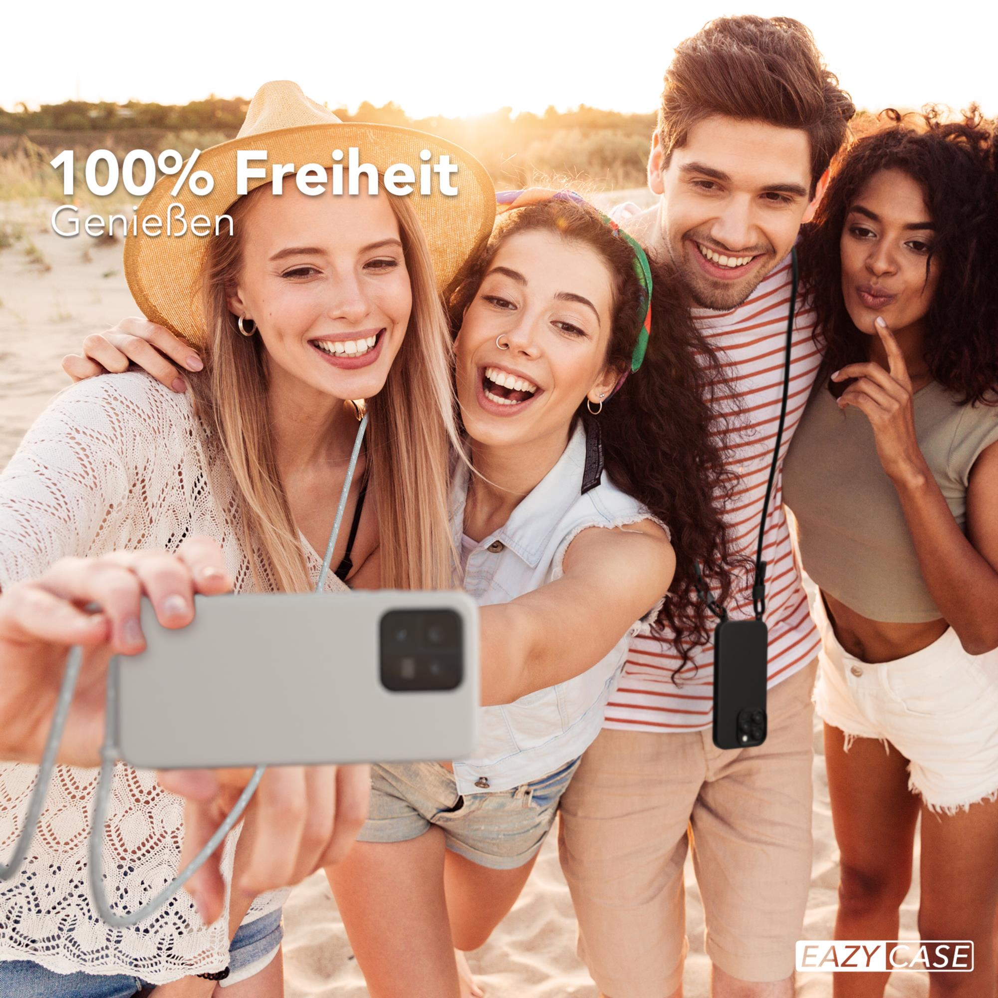 Vier Personen machen ein Selfie am Strand. Eine Person hält ein Telefon. Es gibt einen Sandstrand und Meer im Hintergrund.
