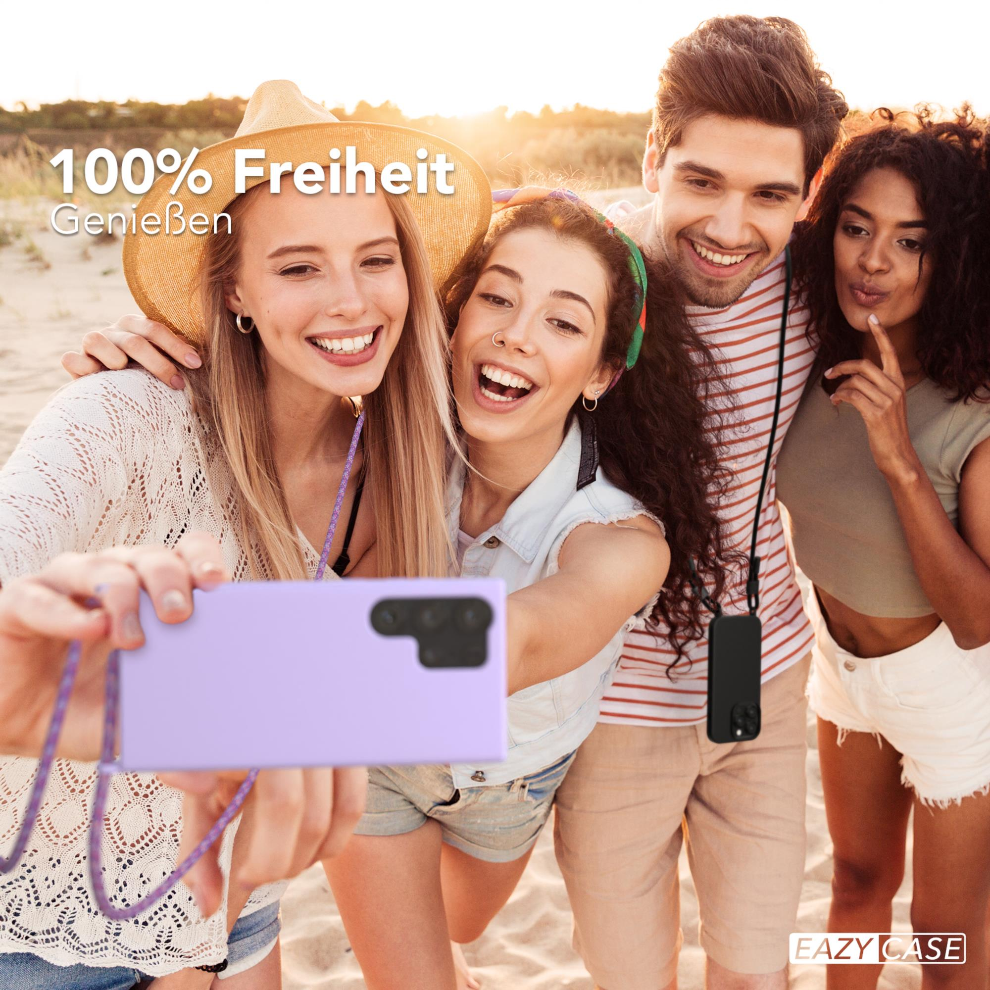Vier Personen machen ein Selfie am Strand. Einer hält ein Telefon mit lila Hülle und lacht.