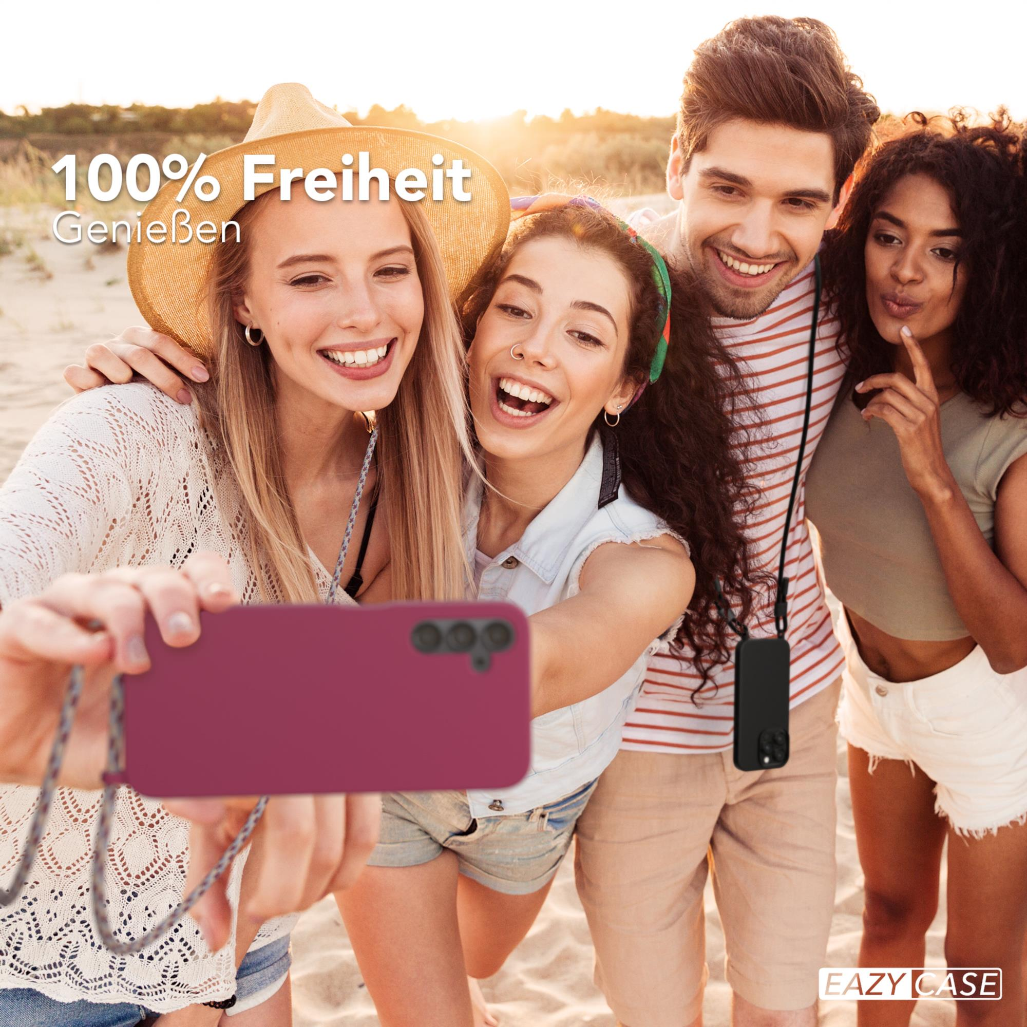 Gruppe von Leuten macht Selfie, mit Telefon in burgunderfarbener Hülle, lächelnd am Strand.