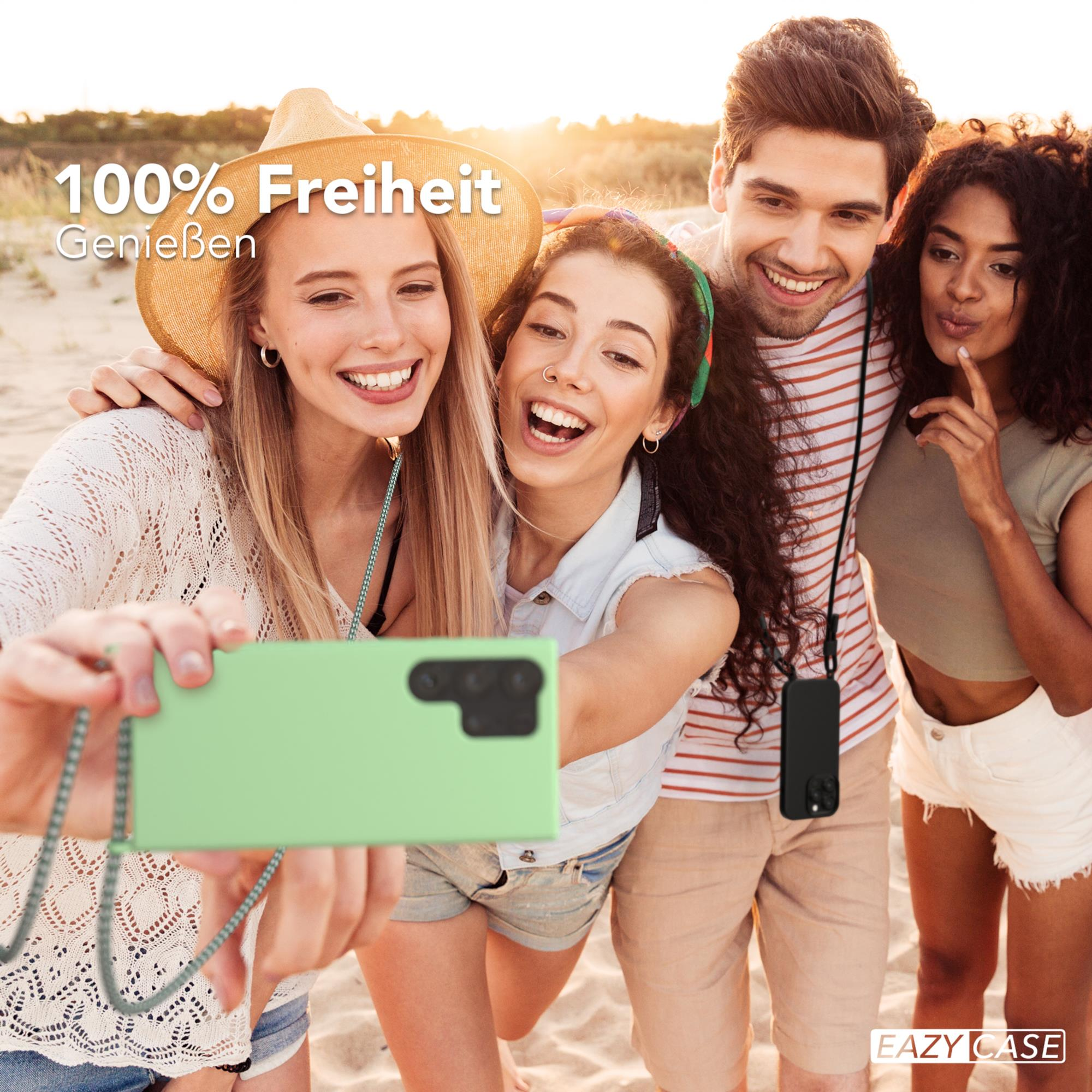 Vier Personen machen ein Selfie am Strand. Eine Person hält ein grünes Telefon mit einem Schlüsselband.