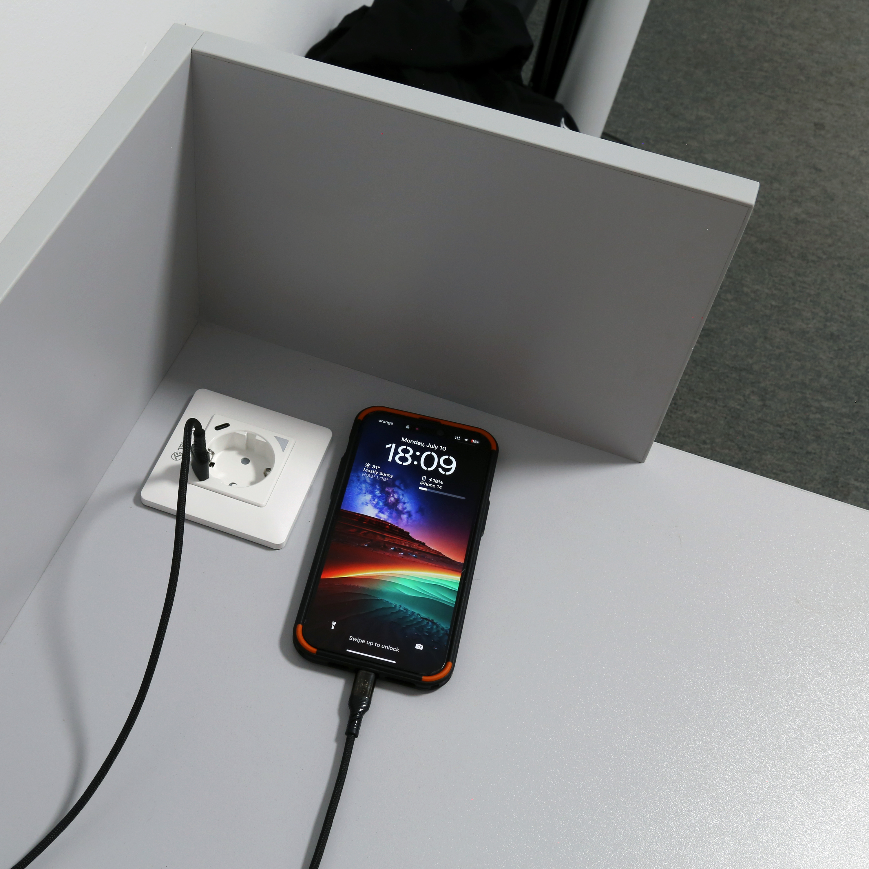 Ein schwarzes Telefon, das über ein Kabel geladen wird, das an eine Steckdose auf einer grauen Oberfläche angeschlossen ist.