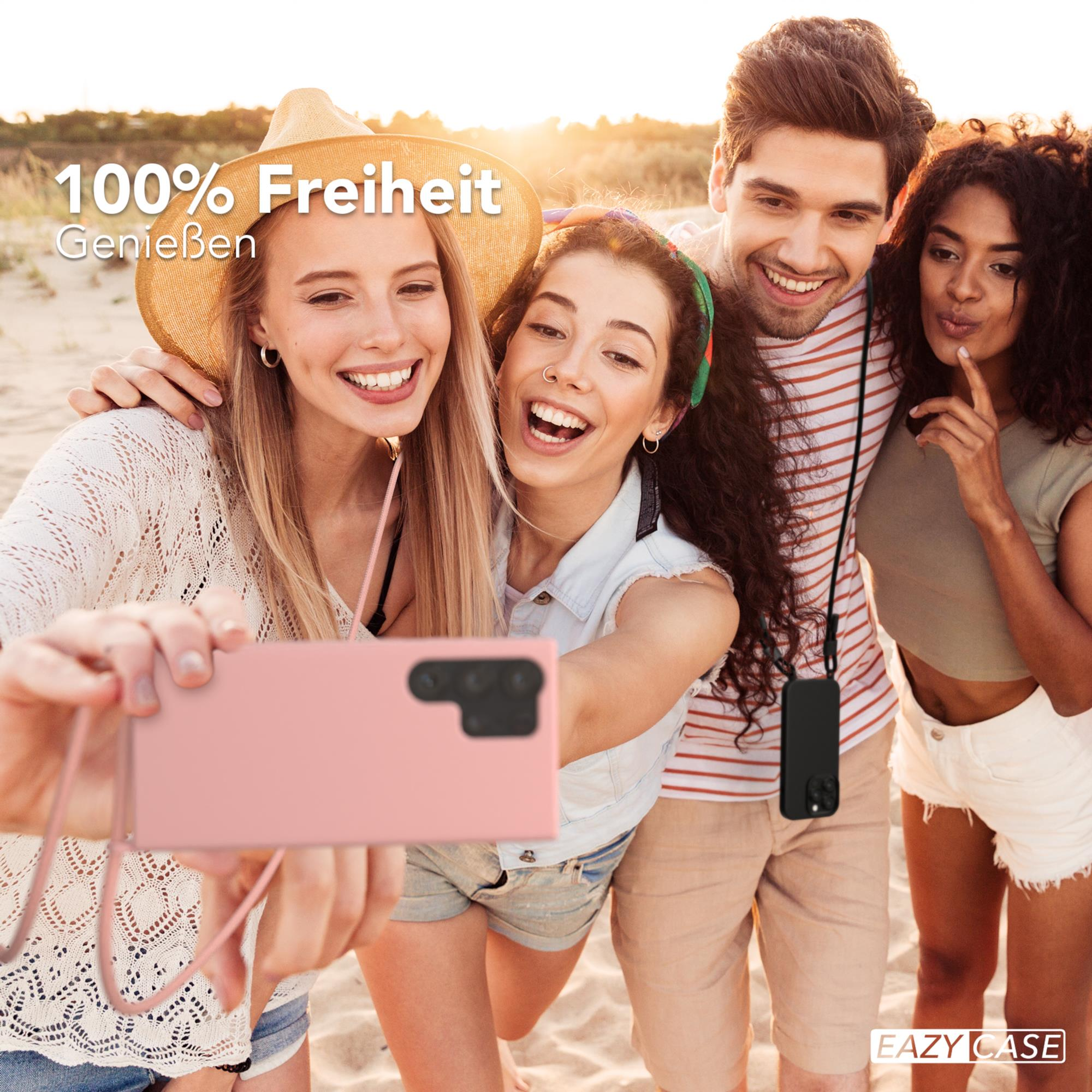 Vier lächelnde Personen machen ein Selfie mit einem rosa Telefon. Strandhintergrund mit Text.