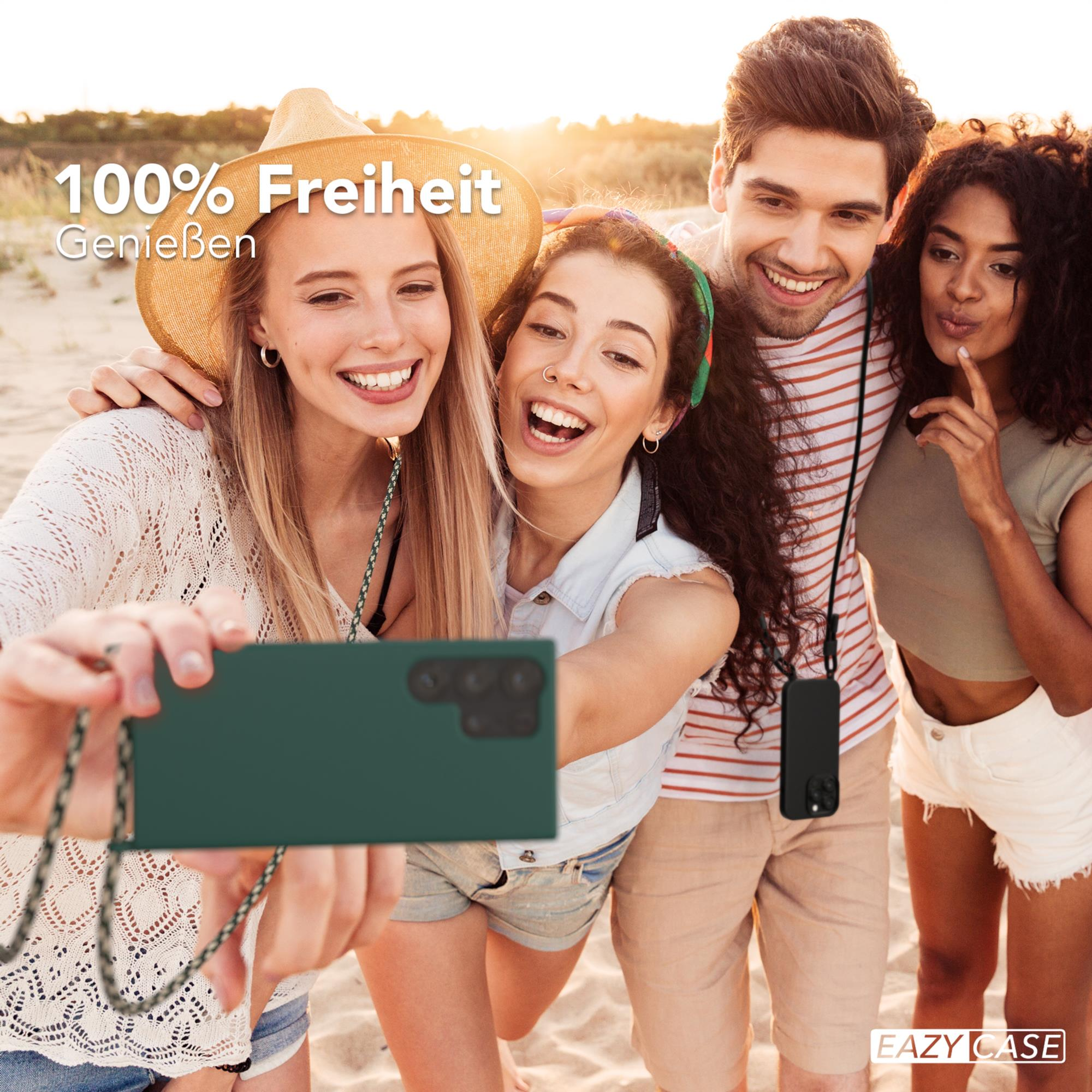 Vier Personen am Strand machen Selfie mit grüner Handyhülle und Lanyard.