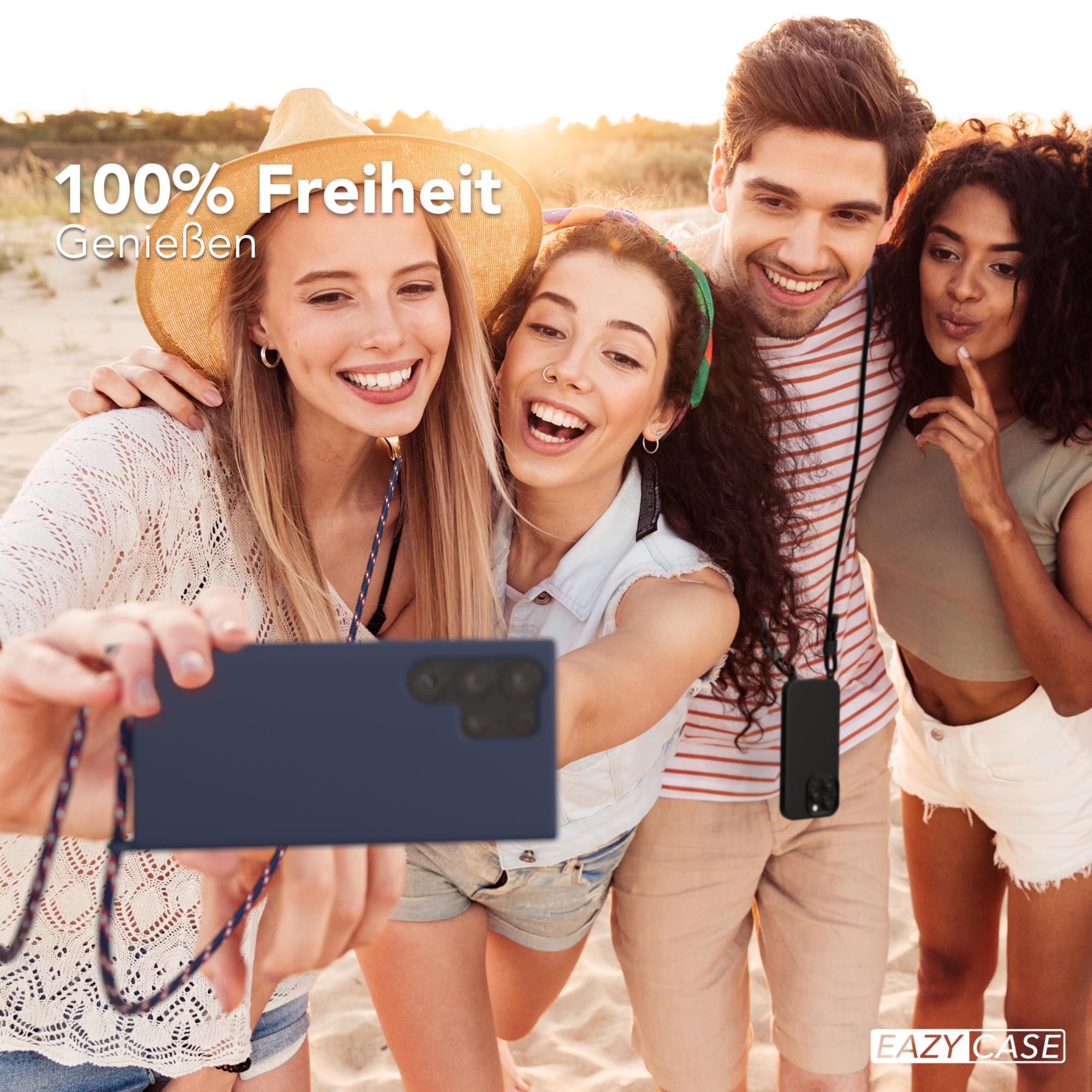 Vierköpfige Gruppe macht Selfie am Strand. Lächeln, halten Telefon mit Hülle und Lanyard. Blauer Ozean im Hintergrund.