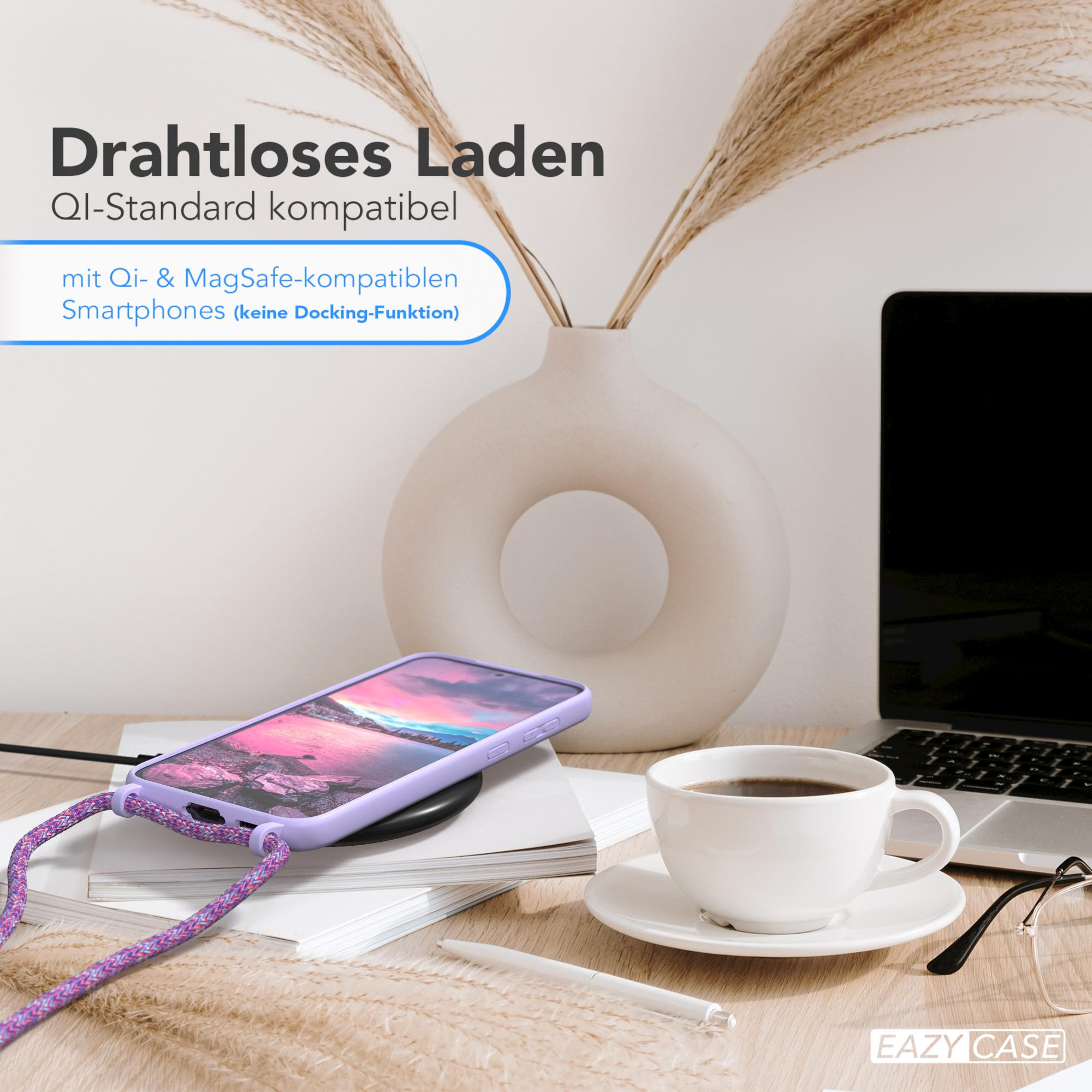 Ein Telefon liegt auf einem kabellosen Ladegerät. Eine Tasse Kaffee, ein Laptop und eine Vase mit getrockneten Pflanzen sind sichtbar.