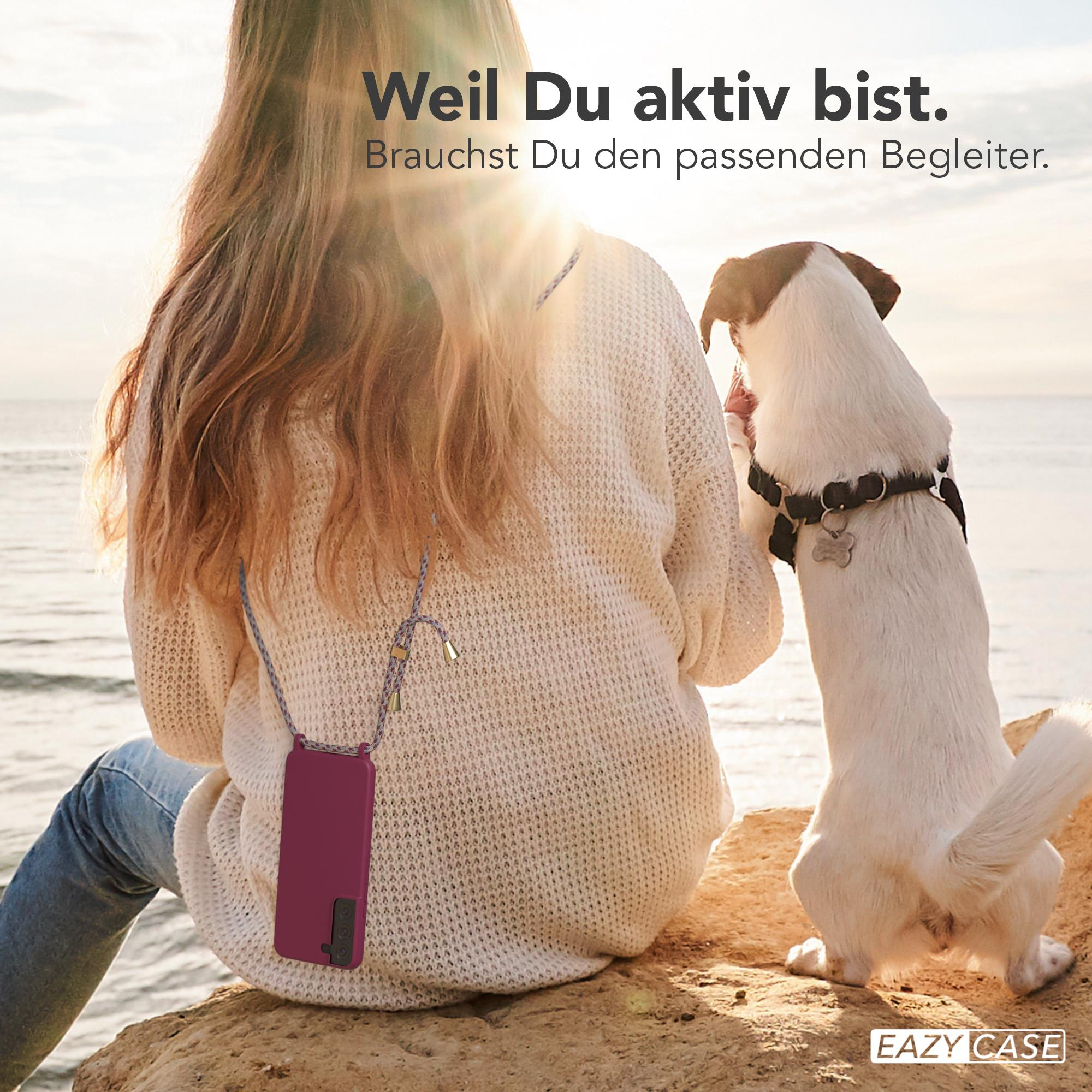Frau am Strand mit Hund, hält Telefon mit Band. Der Hund schaut nach oben.