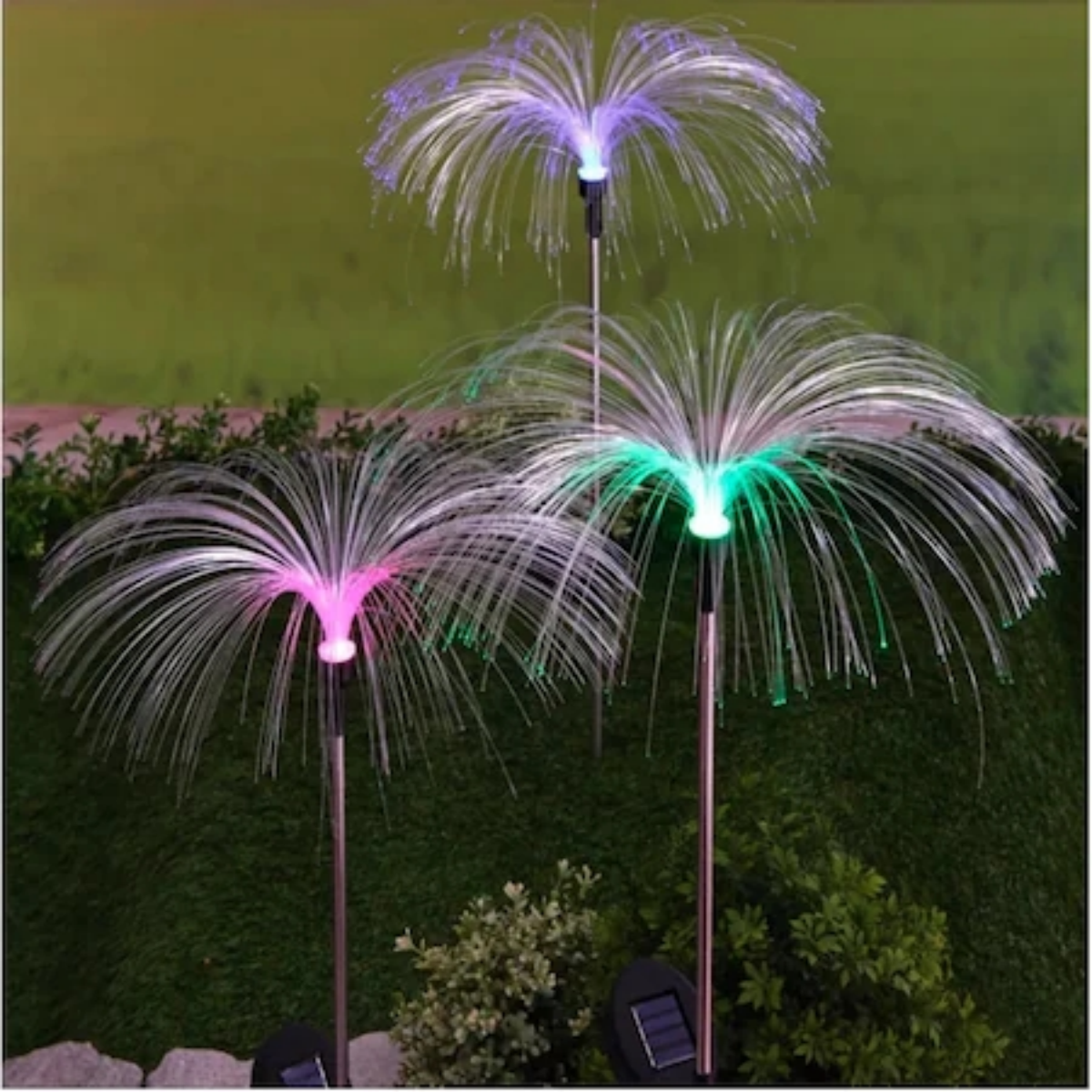 Drei solarbetriebene Gartenleuchten mit bunten, leuchtenden Faseroptik-Blüten auf Rasen.