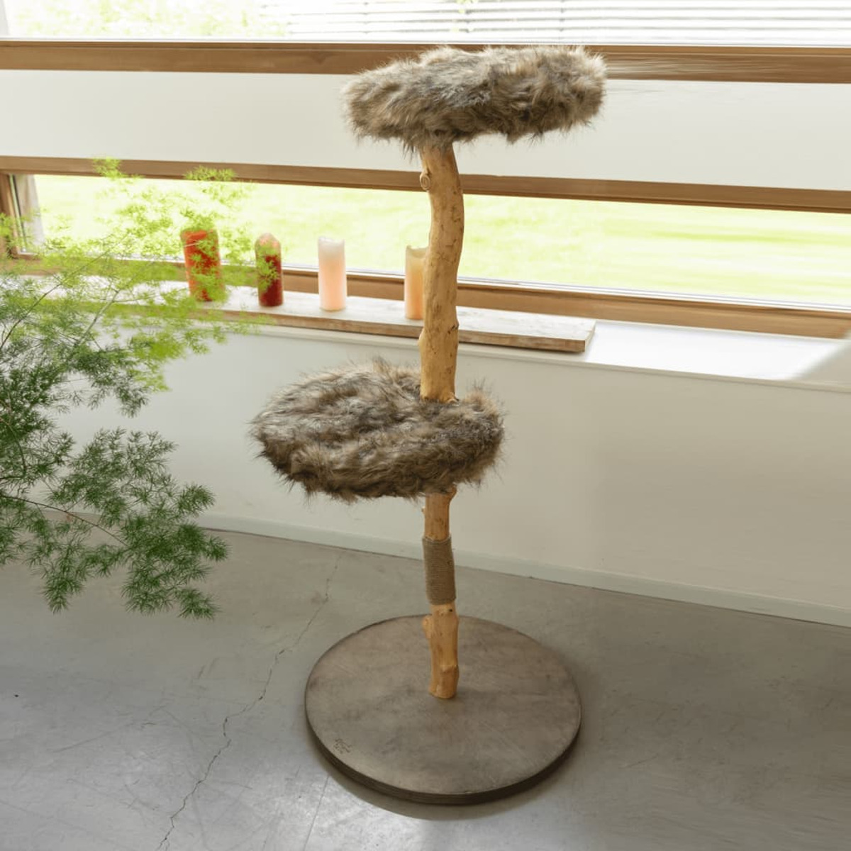 Ein Katzenbaum mit Plattformen, die mit Kunstfell bedeckt sind, neben einem Fenster mit Kerzen.