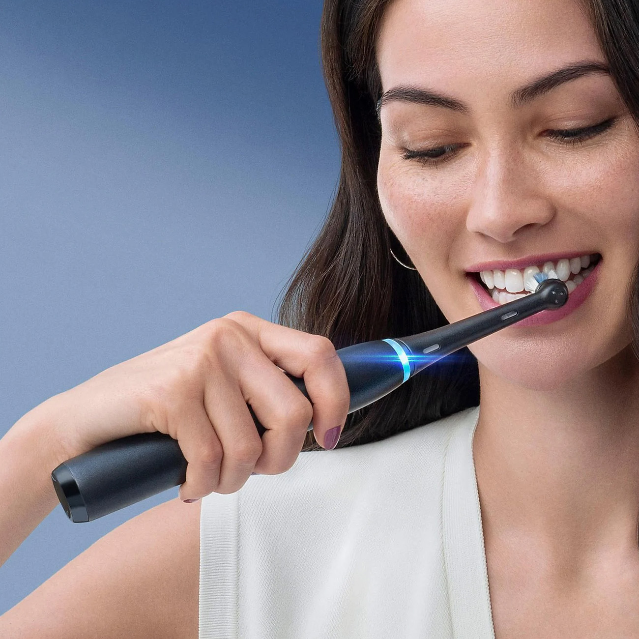 Kobieta szczotkuje zęby czarną elektryczną szczoteczką, zbliżenie. Świeci niebieskie światło.