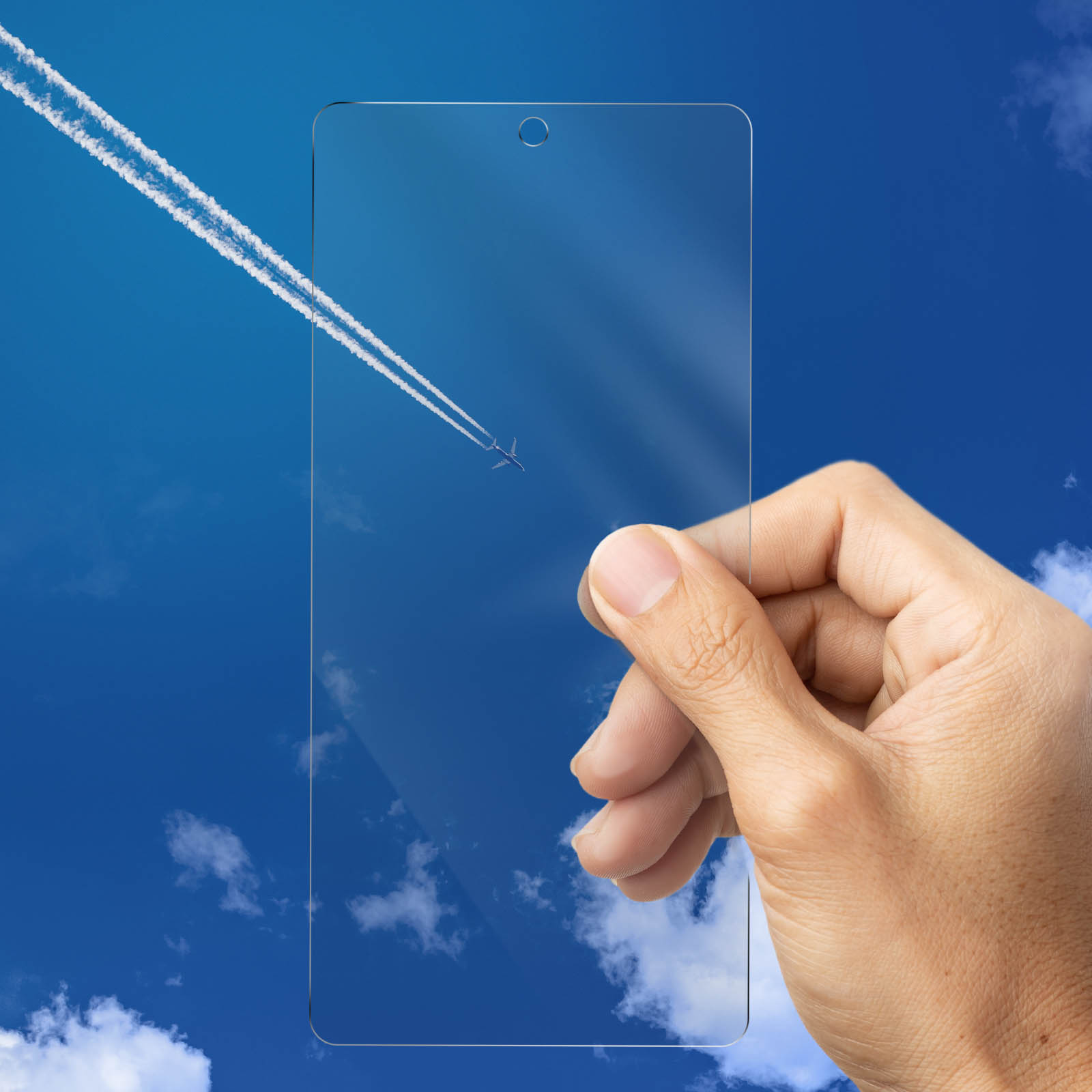 Dłoń trzymająca przezroczystą osłonę ekranu na tle błękitnego nieba ze smugą samolotu.