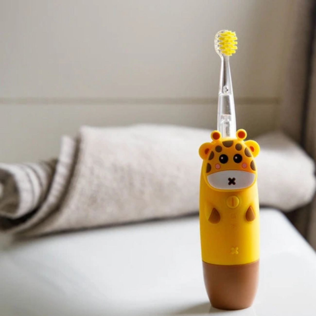 Spazzolino a forma di giraffa giallo con setole gialle, posto su una superficie bianca.