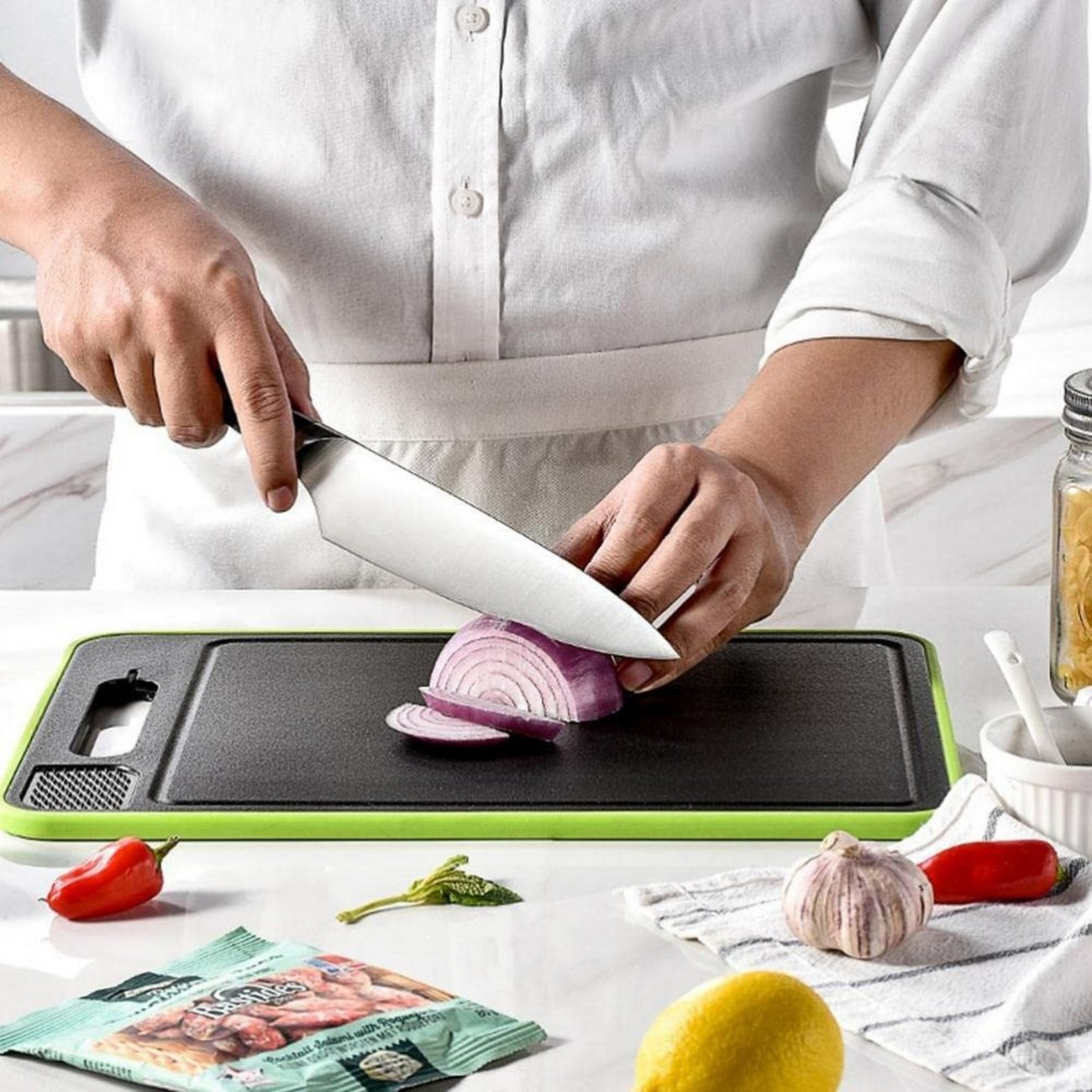 Una persona cortando cebolla roja en una tabla de cortar verde con otros ingredientes.