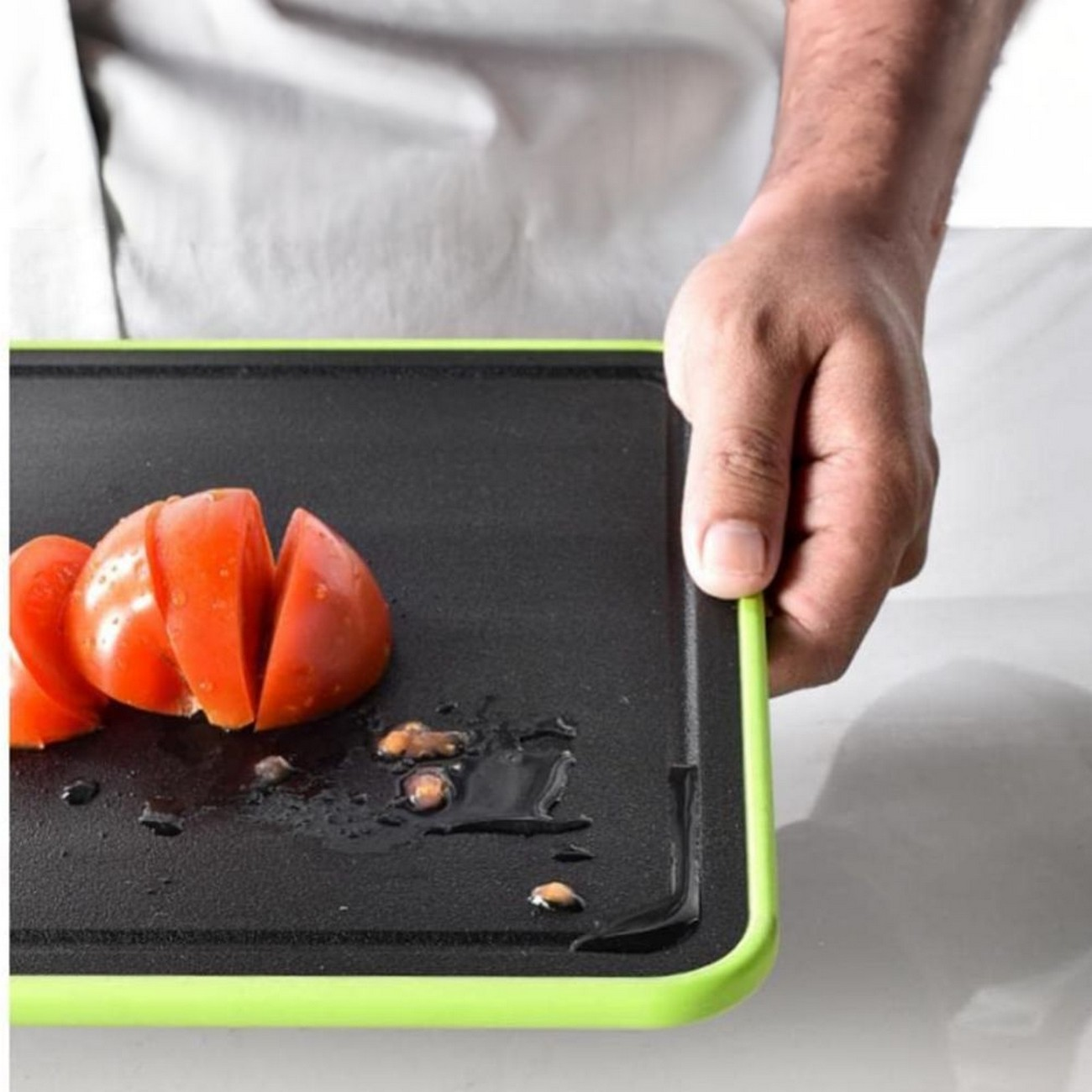 Mano sosteniendo una tabla de cortar verde con tomates en rodajas.