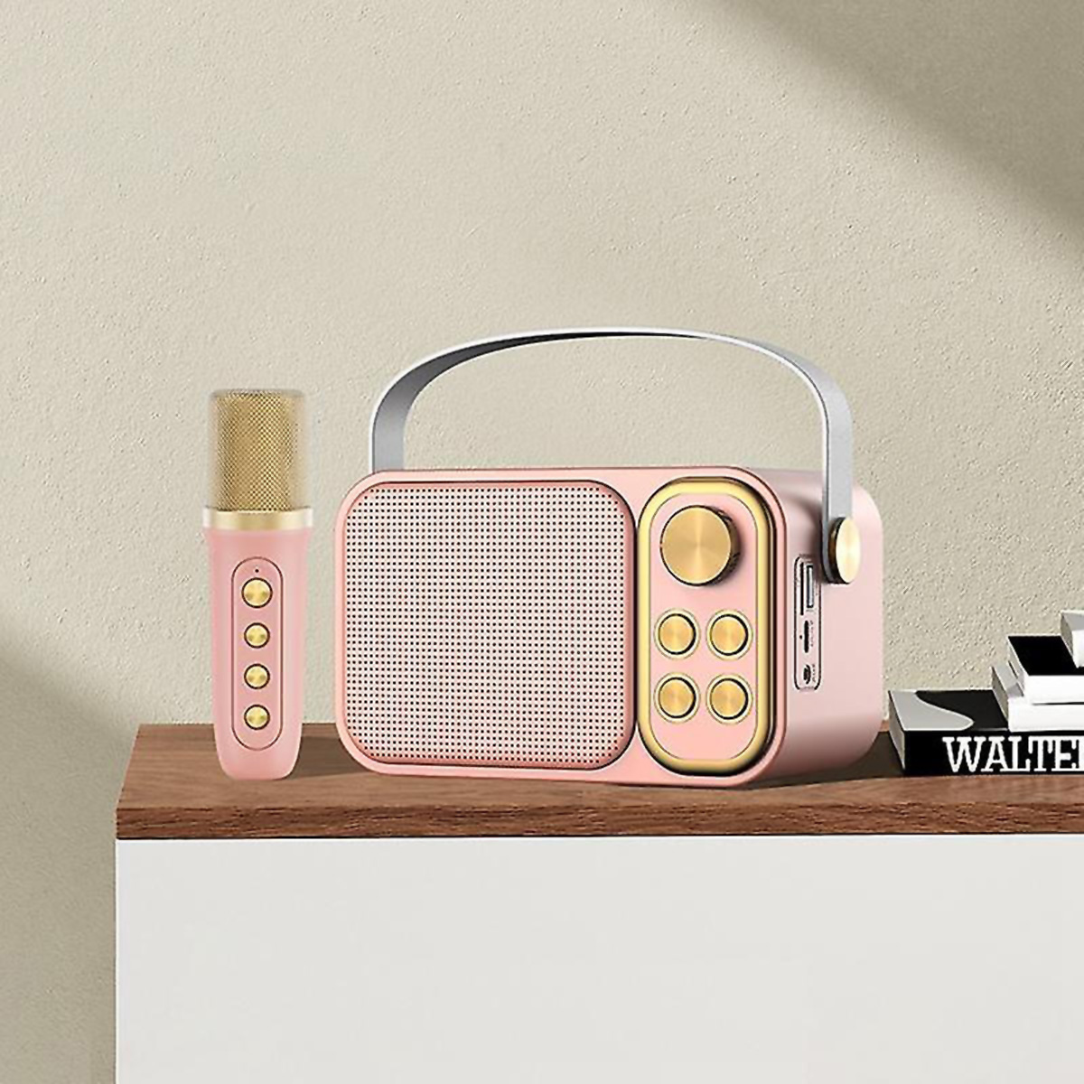 Una radio rosa de estilo retro con un micrófono. Están sobre una superficie de madera, con algunos libros a la derecha.