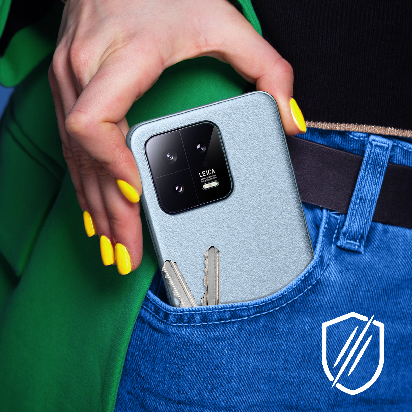 Ręka wkładająca jasno-niebieski telefon do kieszeni. Telefon ma aparat, a w kieszeni są klucze.