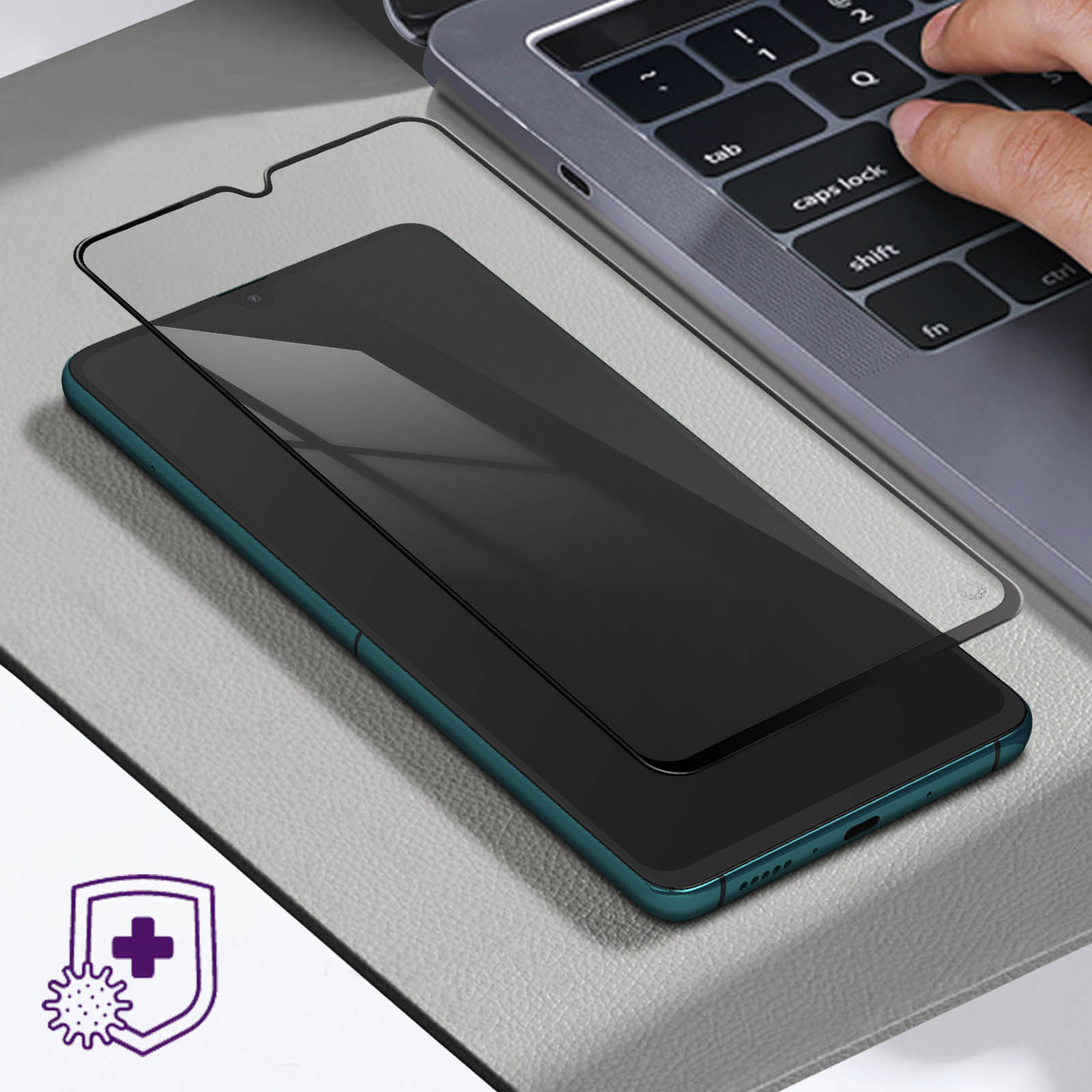 Un telefono con una protezione per lo schermo è su una superficie. Una persona sta digitando su una tastiera di un laptop.